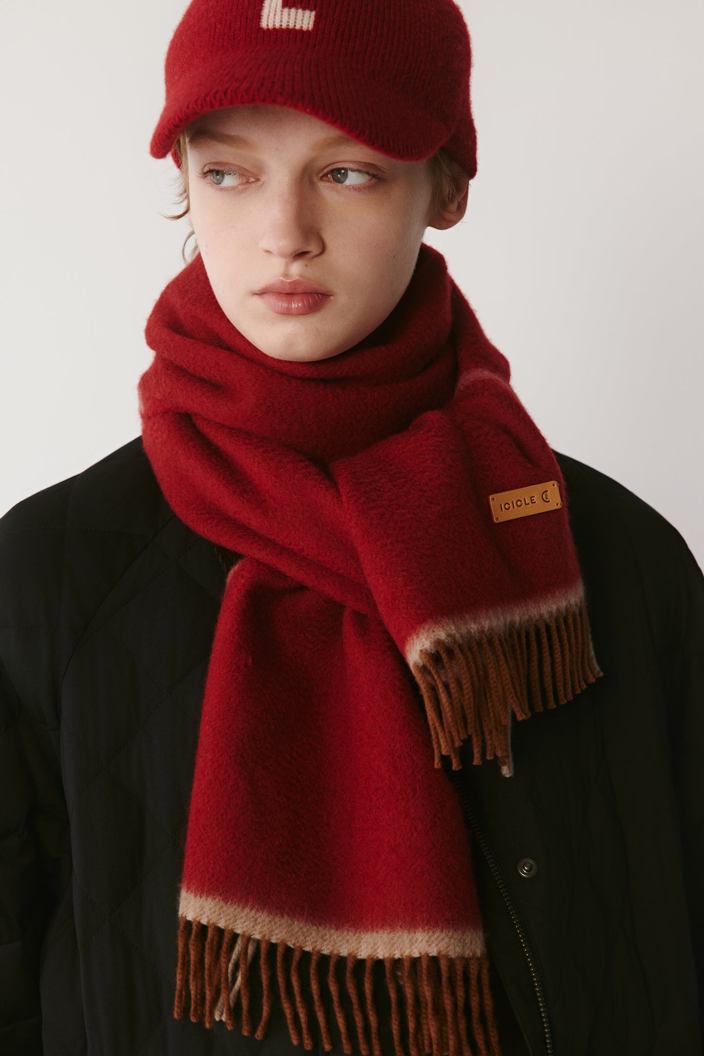 Front view of a red knit scarf and matching cap styled with a black jacket on a light background