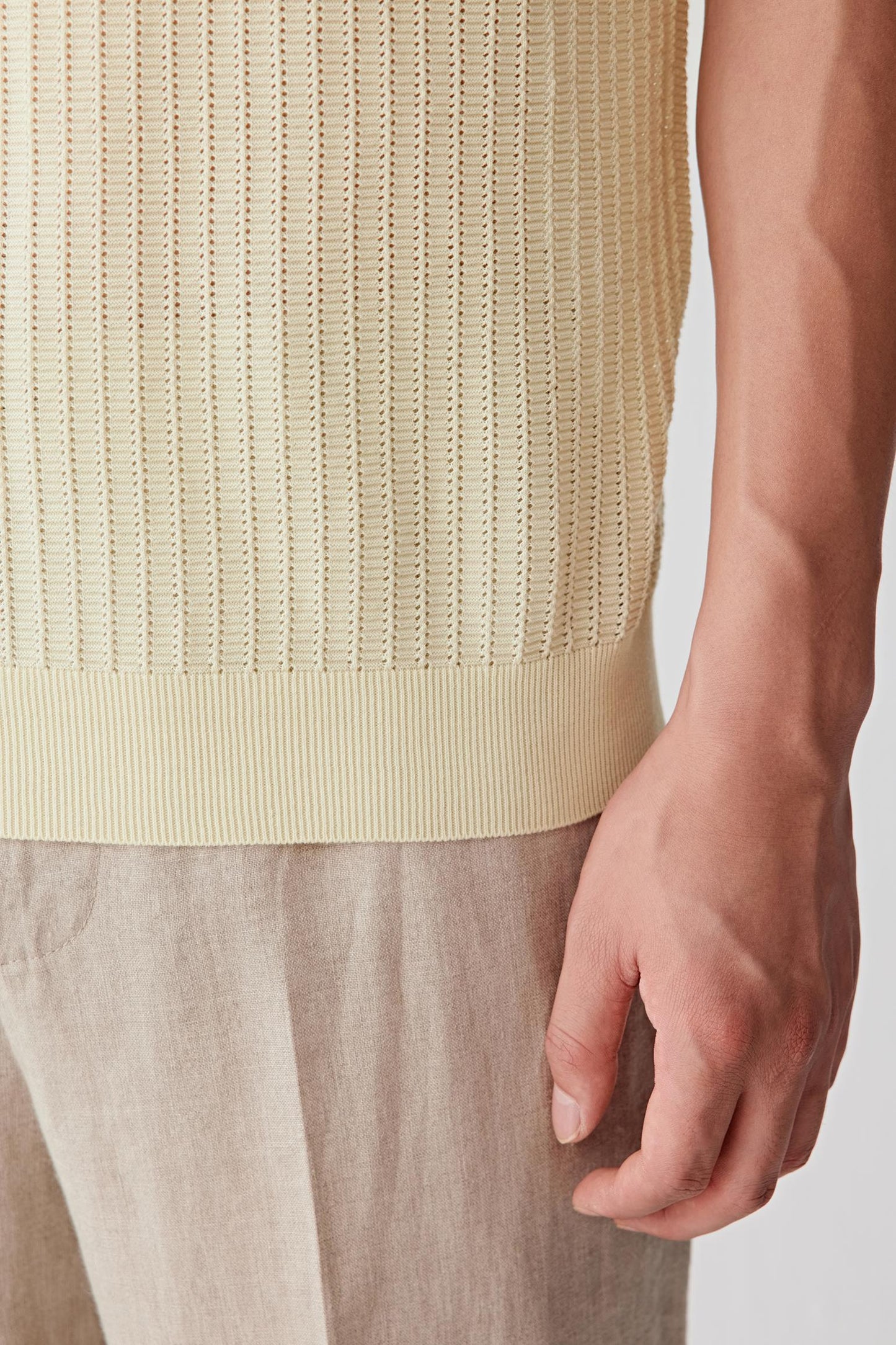 Close-up of the lower body and sleeve area showing the vertical openwork stitch pattern, ribbed finishes and lightweight texture of the cotton knit. The image highlights the depth created by the knit construction and the soft drape of the fabric.