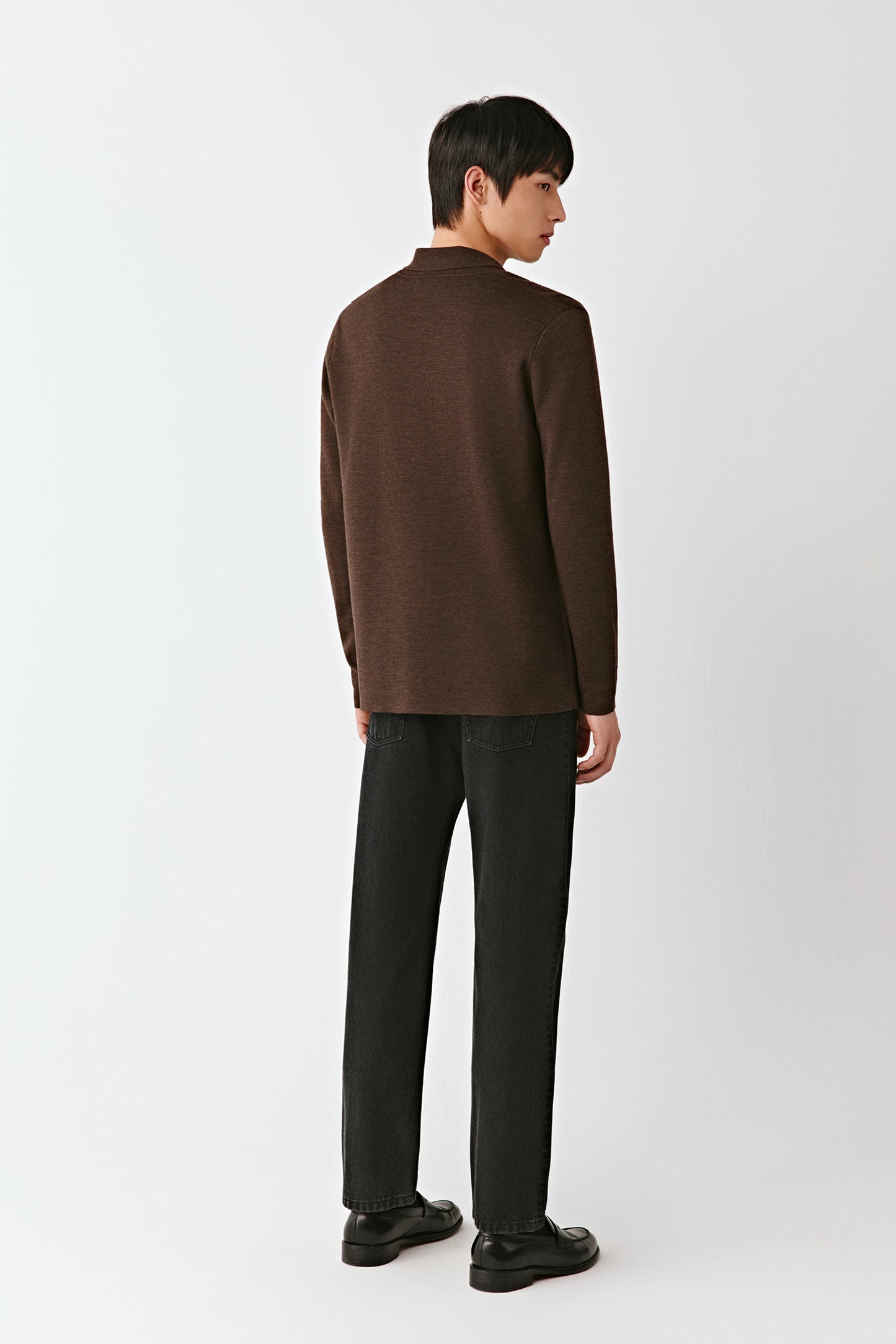 Man wearing a brown sweater and black pants on a white background