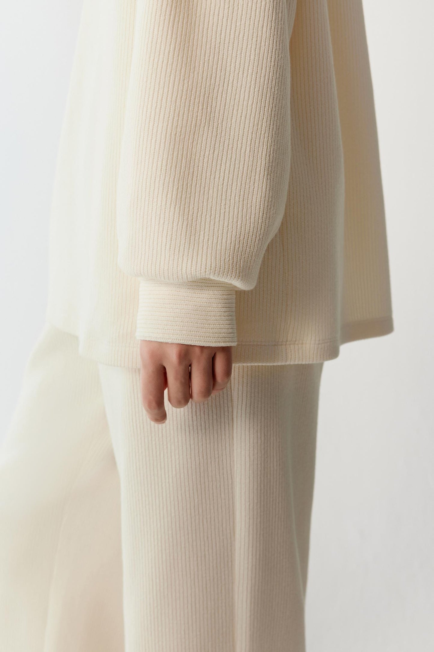 Close-up detail of the sleeve showing the ribbed knit structure and the fluid drape of the fabric.