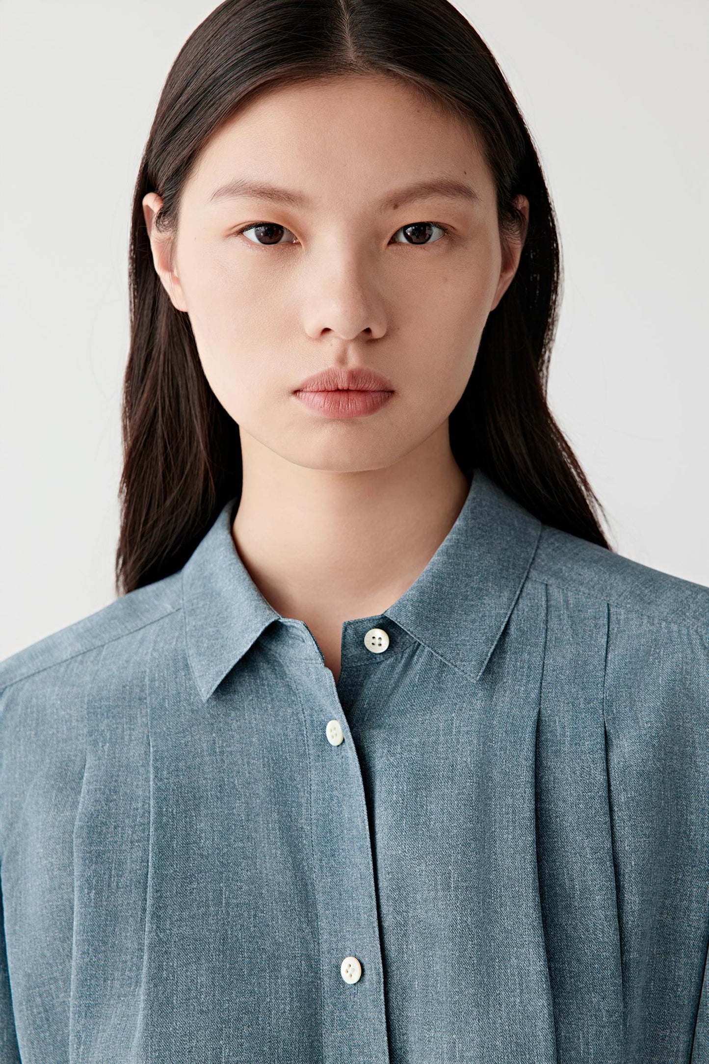 Close-up portrait focusing on the pointed collar and upper placket, emphasizing the concealed fastening, clean finishing and softly textured indigo silk surface