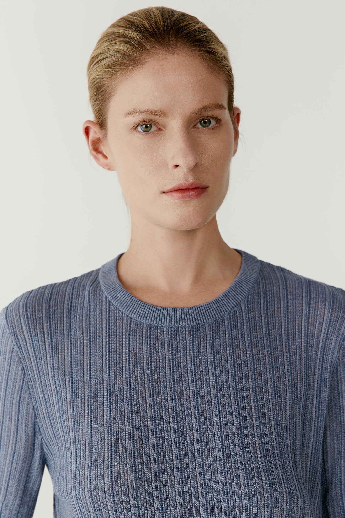 Close-up portrait focusing on the round neckline, upper body construction and ribbed knit surface. The image reveals the fine vertical texture, subtle tonal depth and lightweight appearance characteristic of the linen and silk blend.