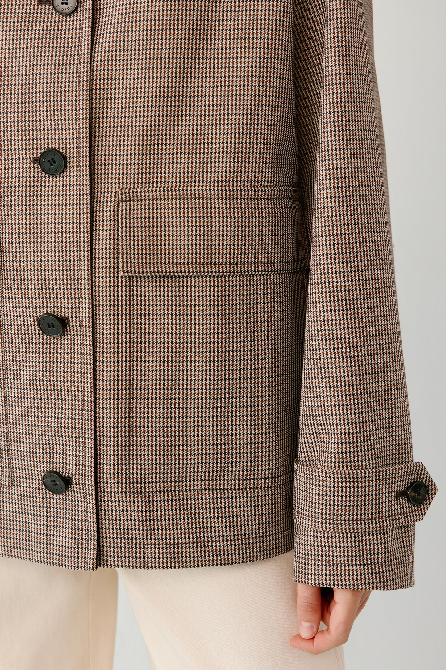Close-up of a brown and beige houndstooth patterned jacket with dark buttons, worn with light beige trousers.