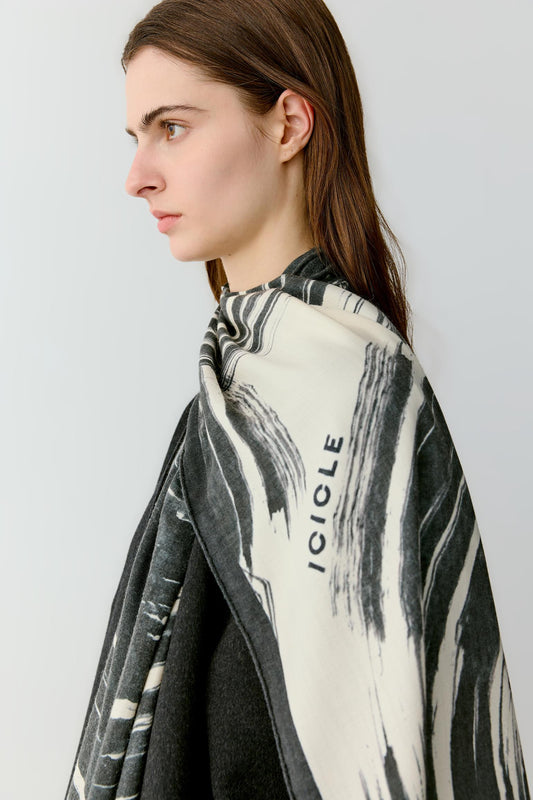 Side view highlighting the fluid drape of the scarf as it falls along the body. The lightweight fabric creates soft folds that reveal the layered graphic pattern.