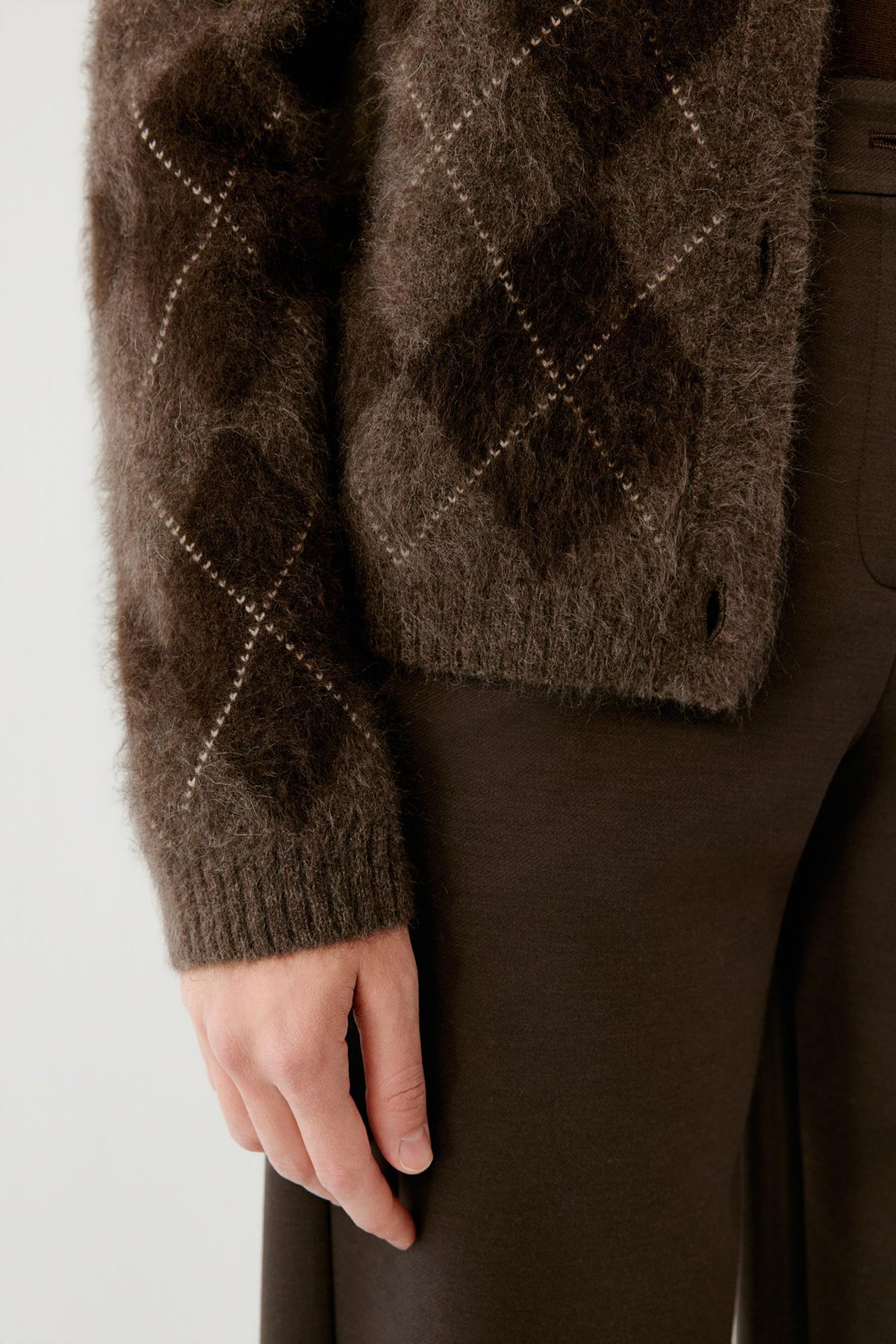 Close-up highlighting the long sleeve, ribbed cuff and contrasting argyle pattern of the dark brown yak cardigan.