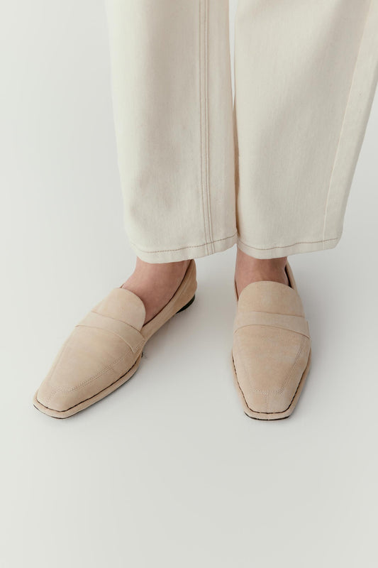 Three-quarter view showing the loafers paired with cream trousers. The gently pointed toe and delicate seamwork create a refined silhouette.