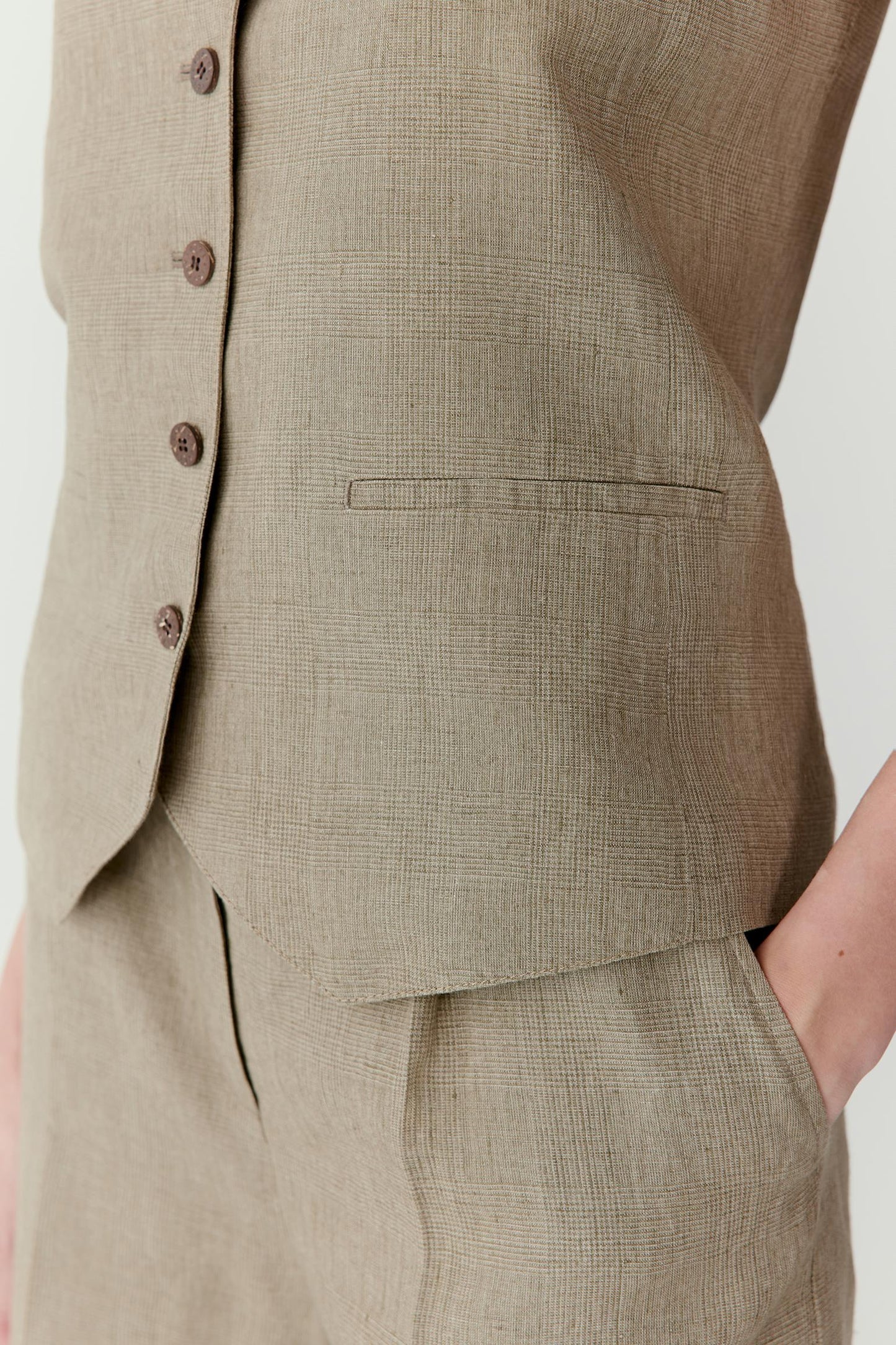 Close-up view of the front panel and fastening area. The image reveals the characteristic irregular texture of undyed linen, the subtle glen plaid pattern, clean seam construction and the refined finish of the buttoned front.