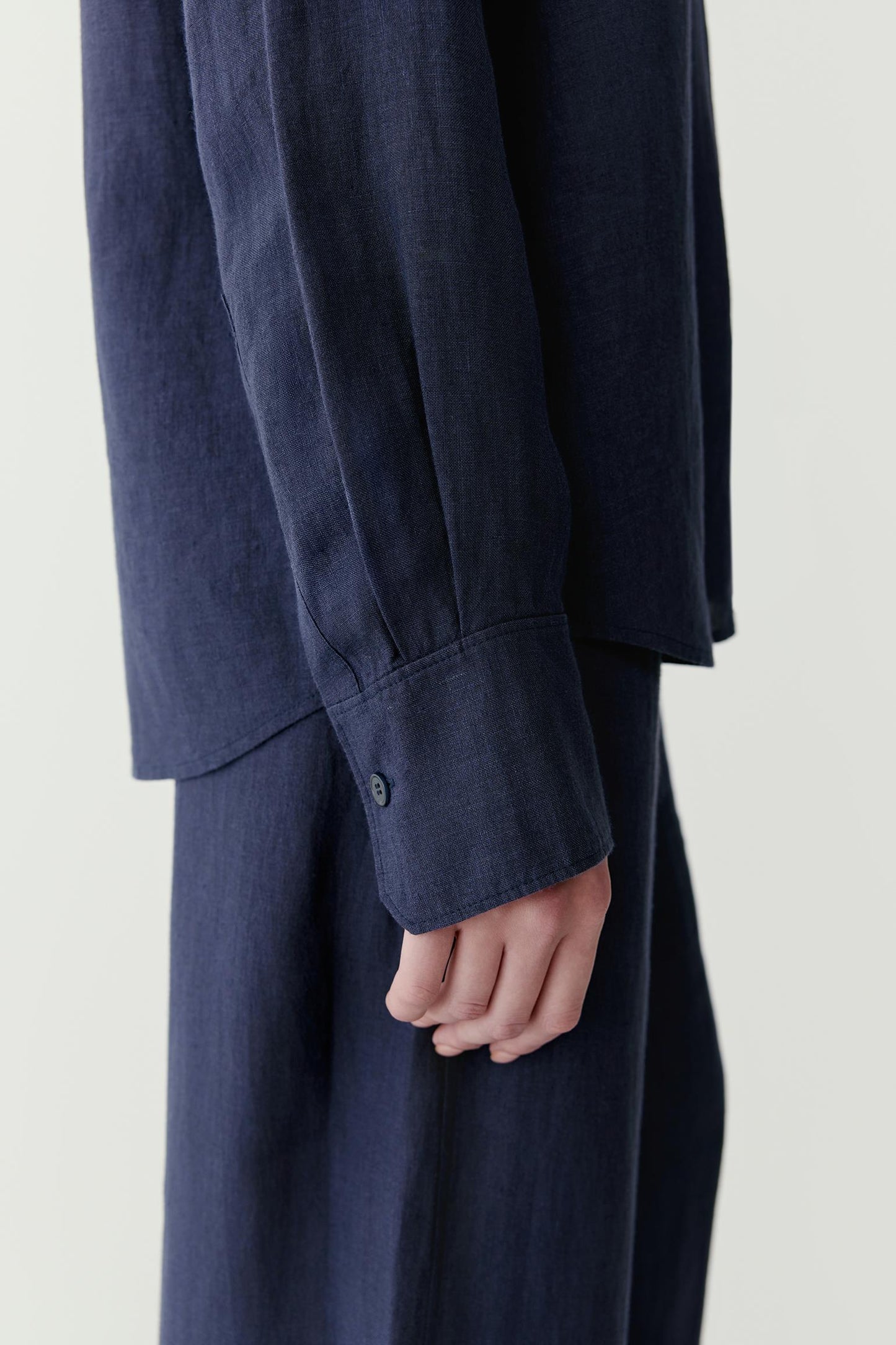 Close-up view focusing on the sleeve and cuff construction. The image reveals the lightly textured linen surface, subtle tonal depth of the navy shade and the clean finishing that defines the garment.