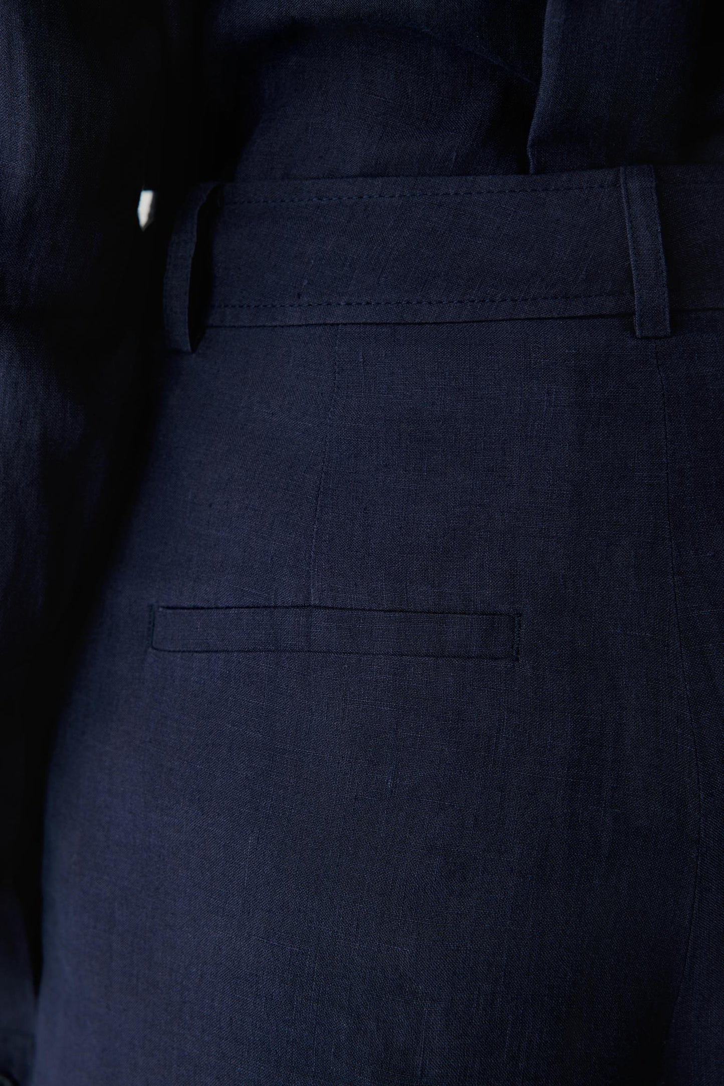 Close-up view focusing on the side pocket area and fabric surface. The image showcases the characteristic texture of linen, the clean finishing and the fluid structure that shapes the silhouette.