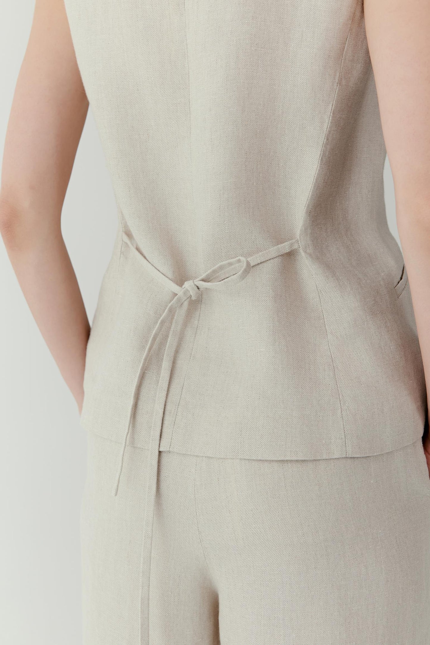 Close-up view of the waist and side construction detailing the dart shaping, seam placement and fitted silhouette. The image showcases the characteristic irregular texture of undyed linen, the soft natural beige tone and the refined finishing of the garment.