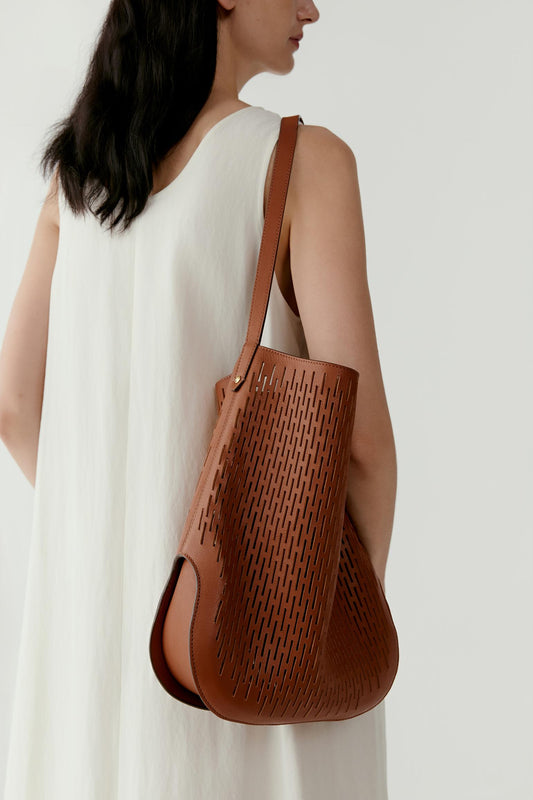 Front view of a model carrying the perforated leather hobo bag on the shoulder. The soft, curved silhouette rests naturally against the body while the perforated surface creates a subtle geometric texture.