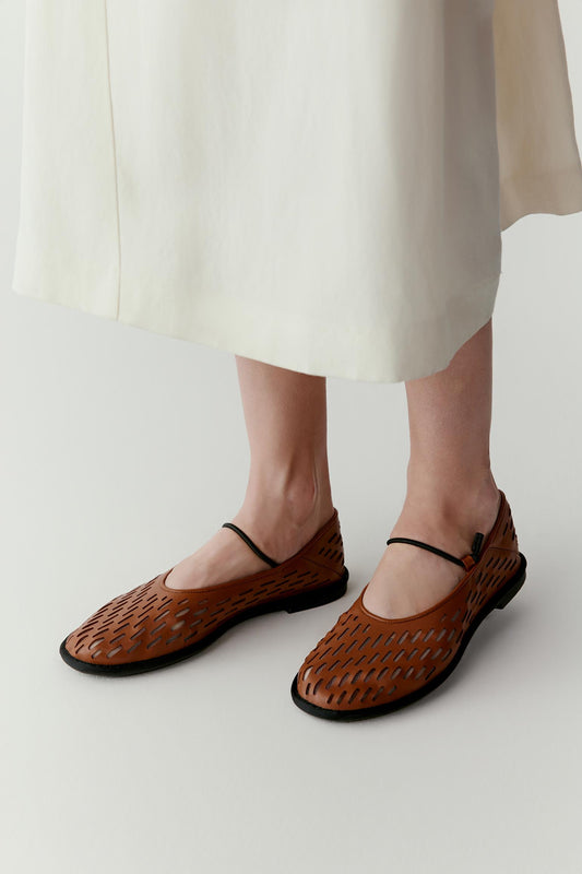 Three-quarter view showing the ballerinas worn with a long, flowing skirt. The warm brown leather contrasts softly with the light fabric while the perforated pattern becomes more visible.