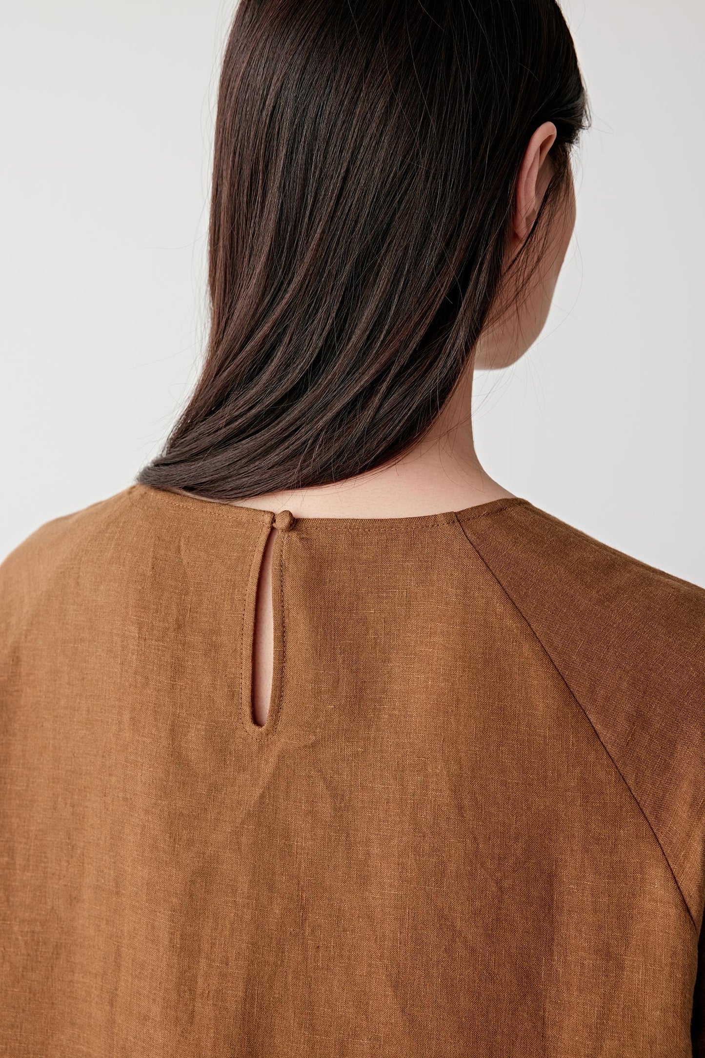 Close-up portrait focusing on the back neckline and upper body, detailing the soft texture, subtle tonal depth and lightweight woven structure of the linen surface