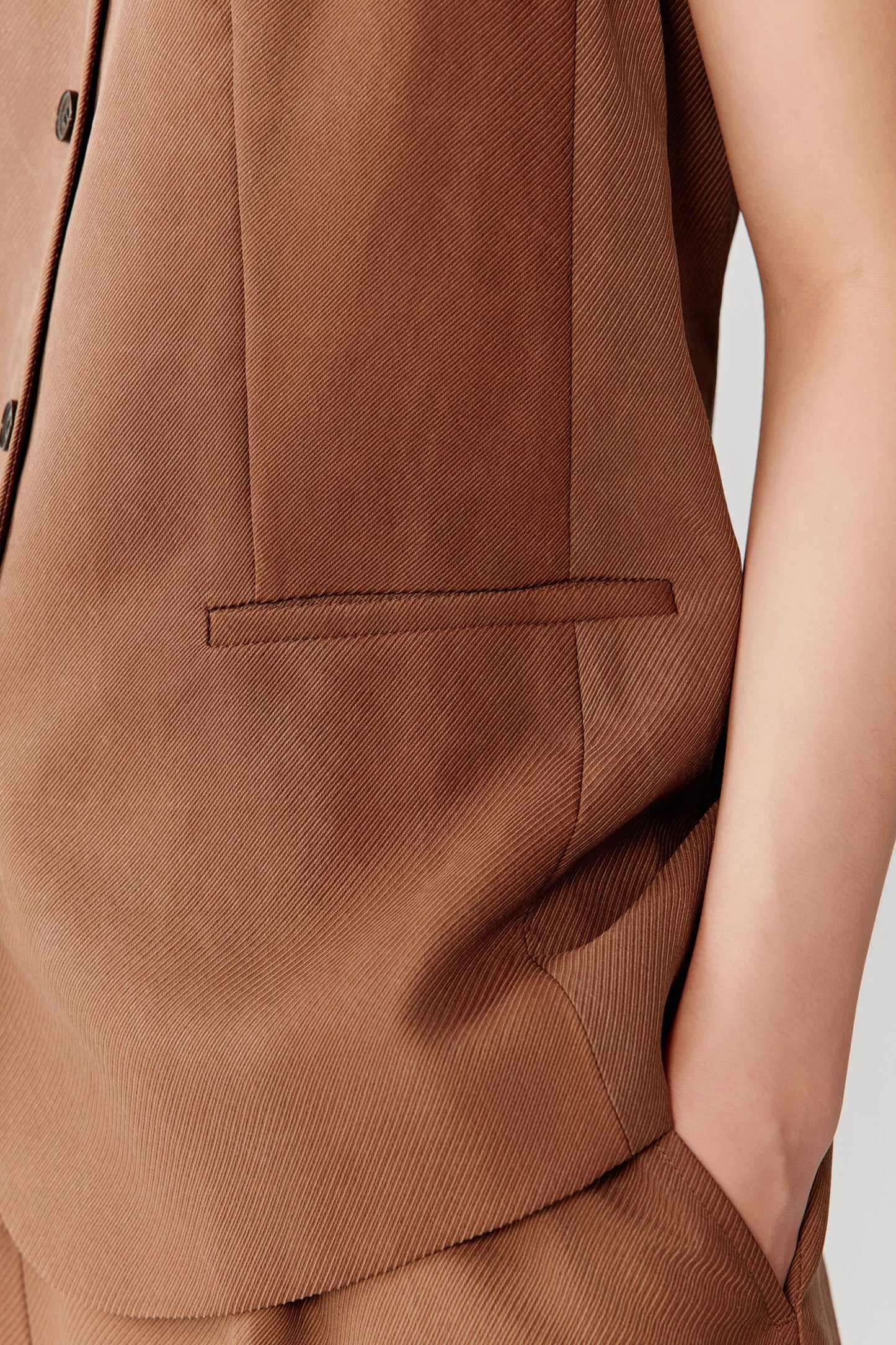 Close-up of pocket and lower front construction showing the patch pocket detail, visible stitching and lightly textured warm brown woven surface with a matte finish
