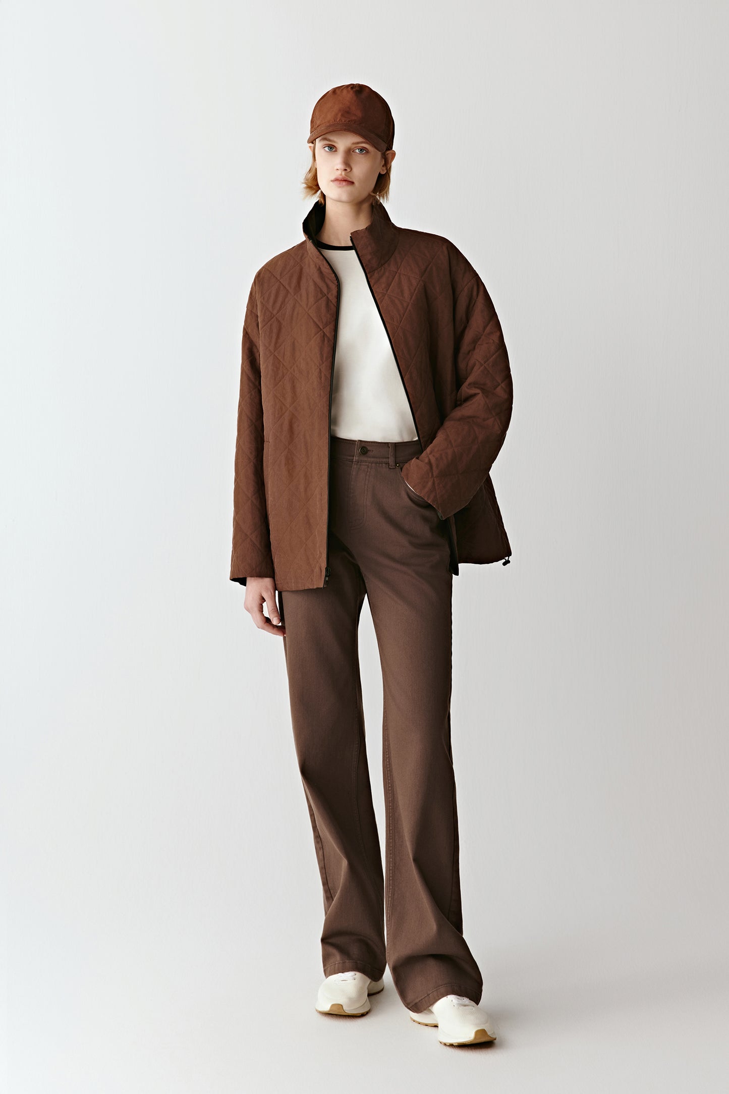Full-length front view of a woman wearing a sienna brown quilted silk jacket with tonal trousers, creating a warm seasonal look.