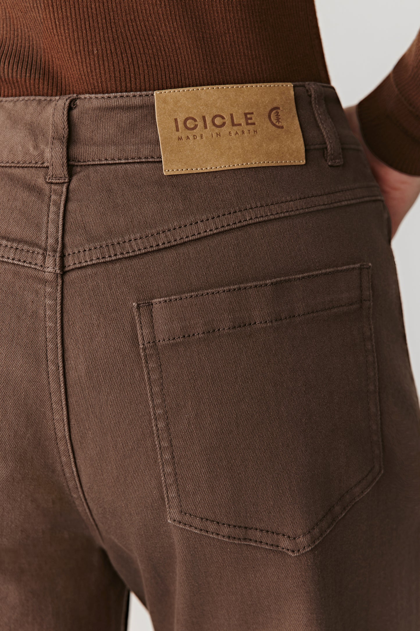A close-up reveals the rich brown shade and the soft matte texture of the low-impact dyed denim.