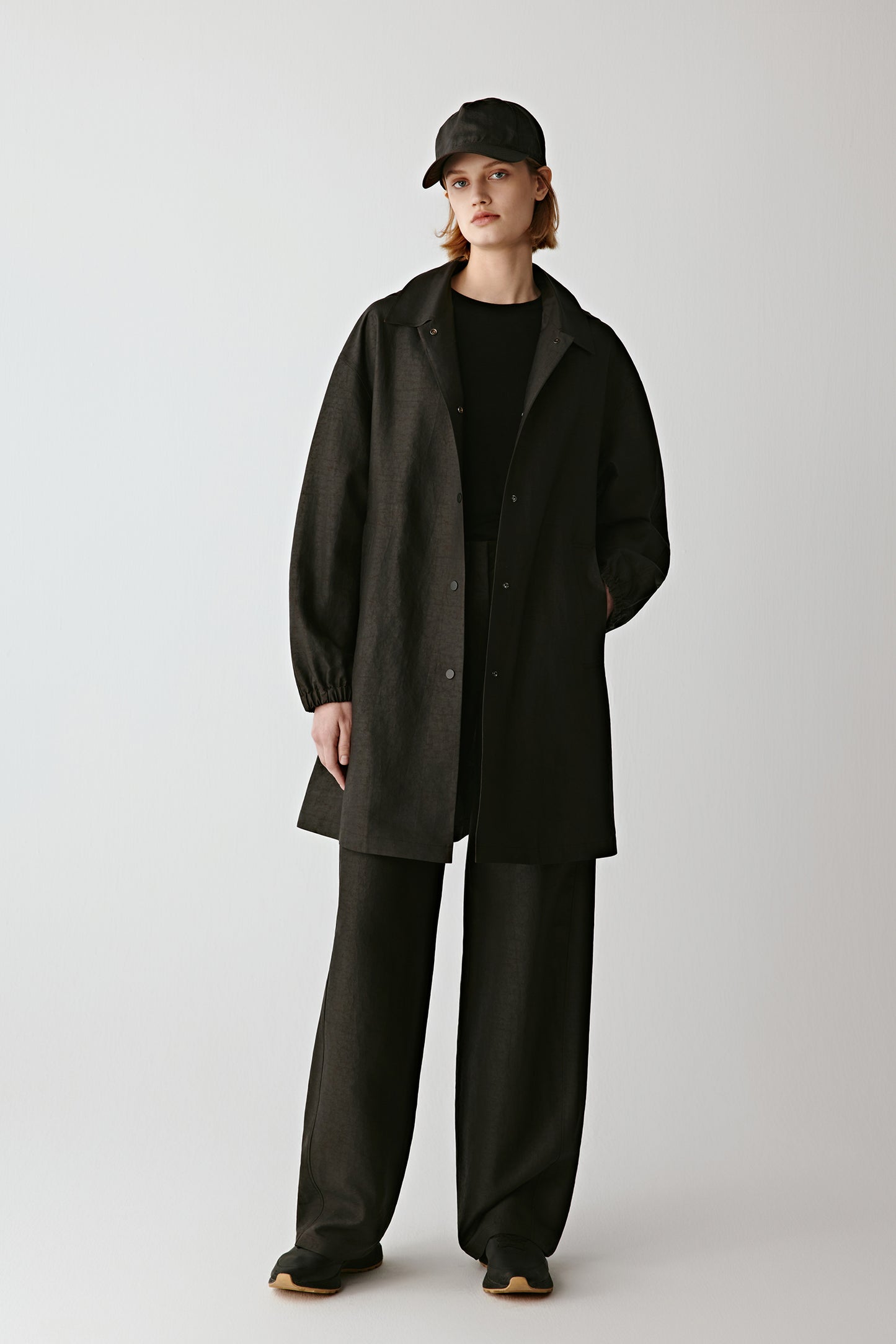 Full-length front view of a woman wearing a long black silk parka with loose trousers for a relaxed contemporary look.
