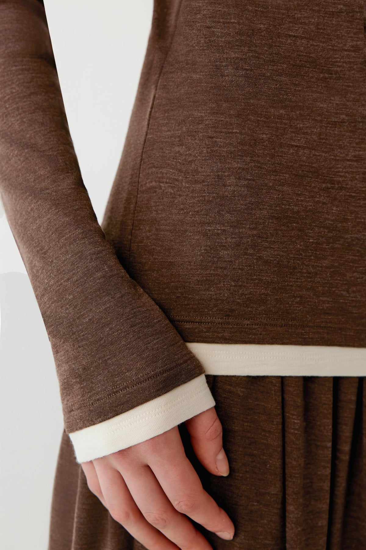 Close-up of a person wearing a brown long-sleeve knit top or dress with a contrasting cream ribbed hem and cuff.