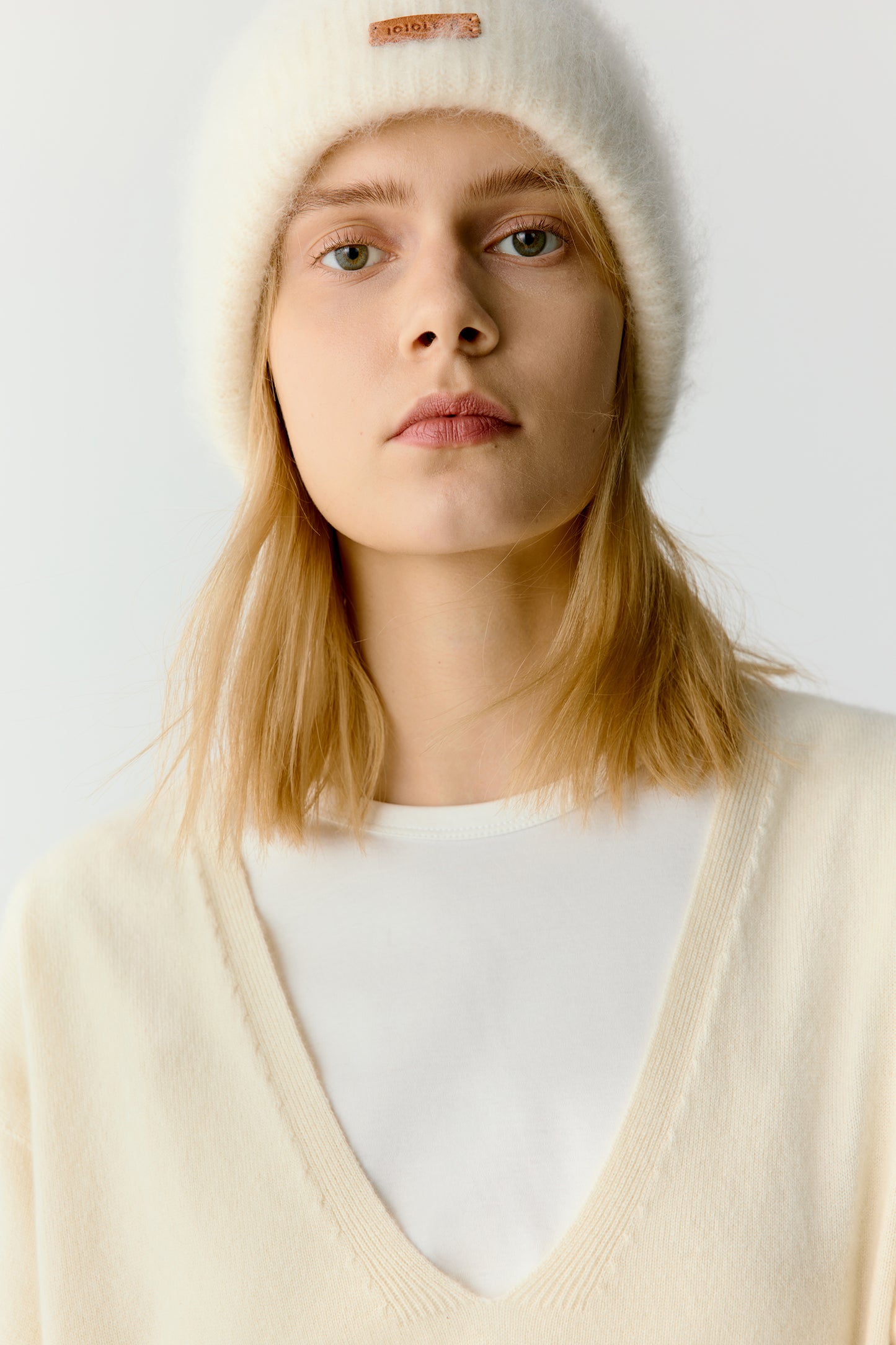 Front view of a woman wearing a white knit beanie and cream sweater on a light background