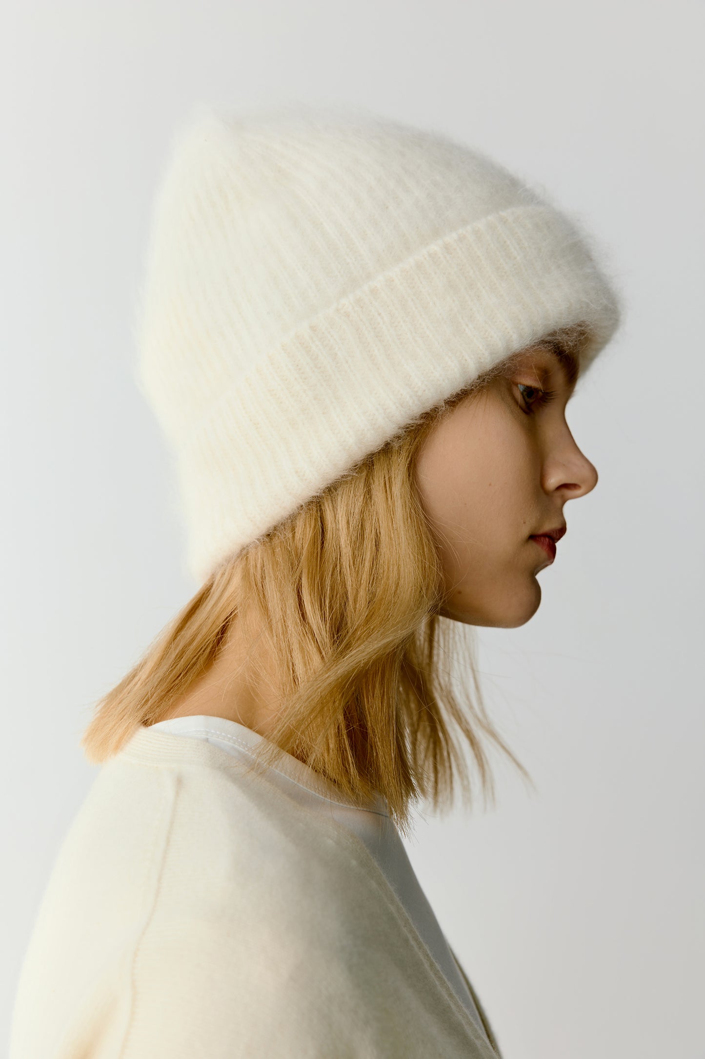 Side view of a woman wearing a white knit beanie on a light background