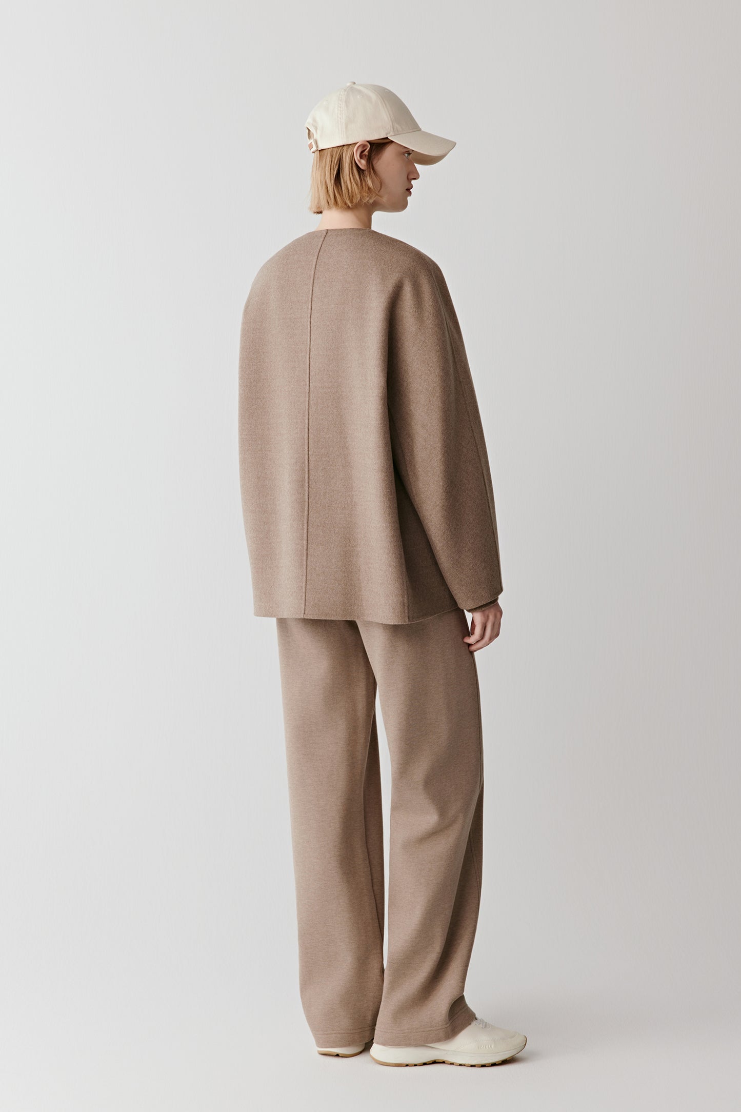 Full back view highlighting the clean vertical line of the coat and its soft structured drape to mid-thigh.