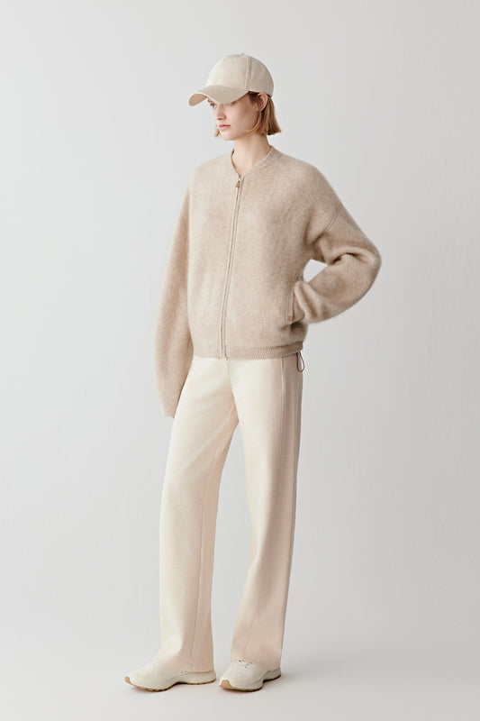 Model dressed in a natural beige undyed cashmere cardigan styled with matching trousers, photographed in soft light. The look conveys quiet luxury and comfort.