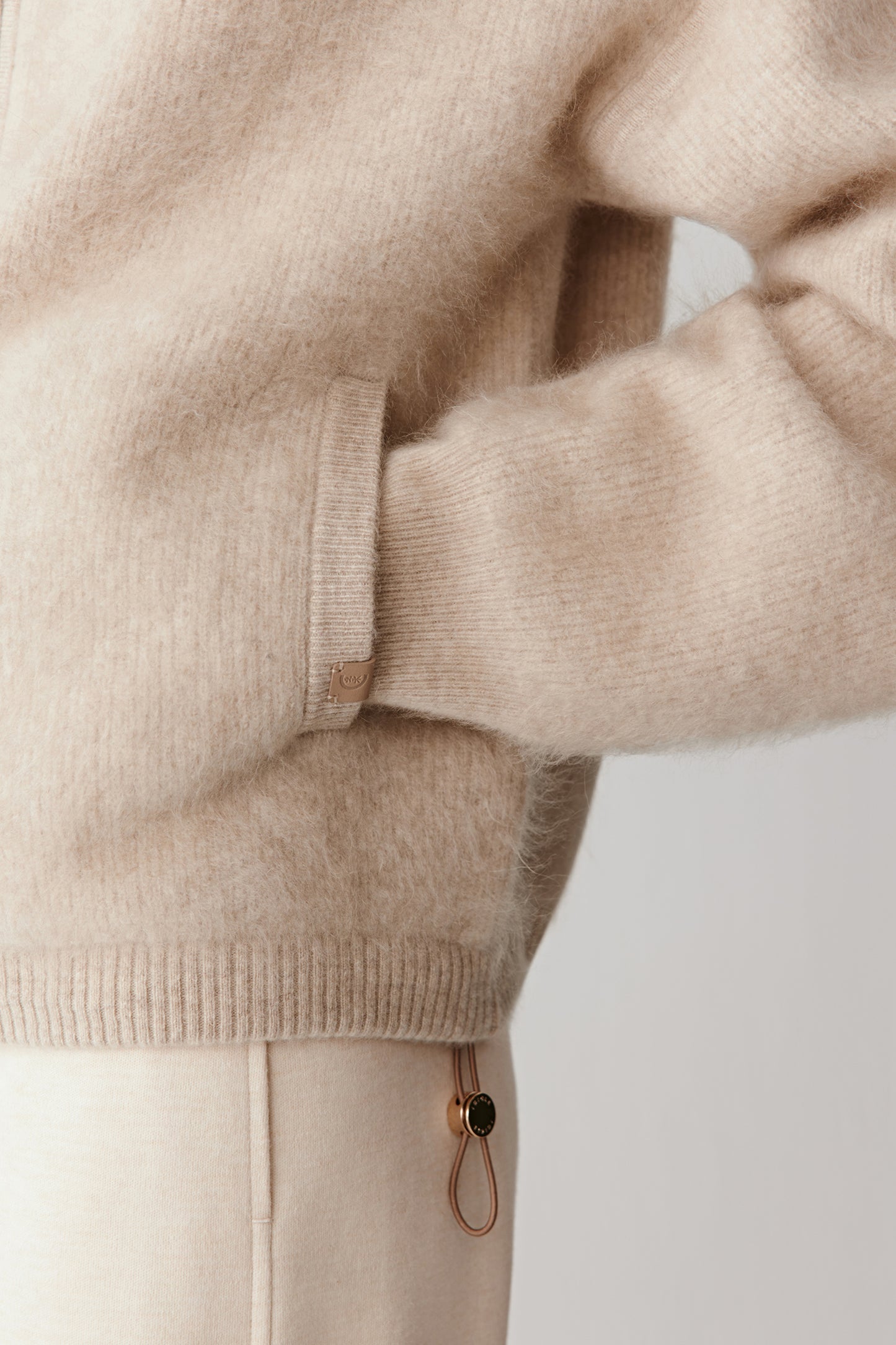 Detailed view of the lower sleeve and side pocket showing the ribbed cuffs and subtle surface texture. The image captures the brushed handfeel and refined finishing of the knit.