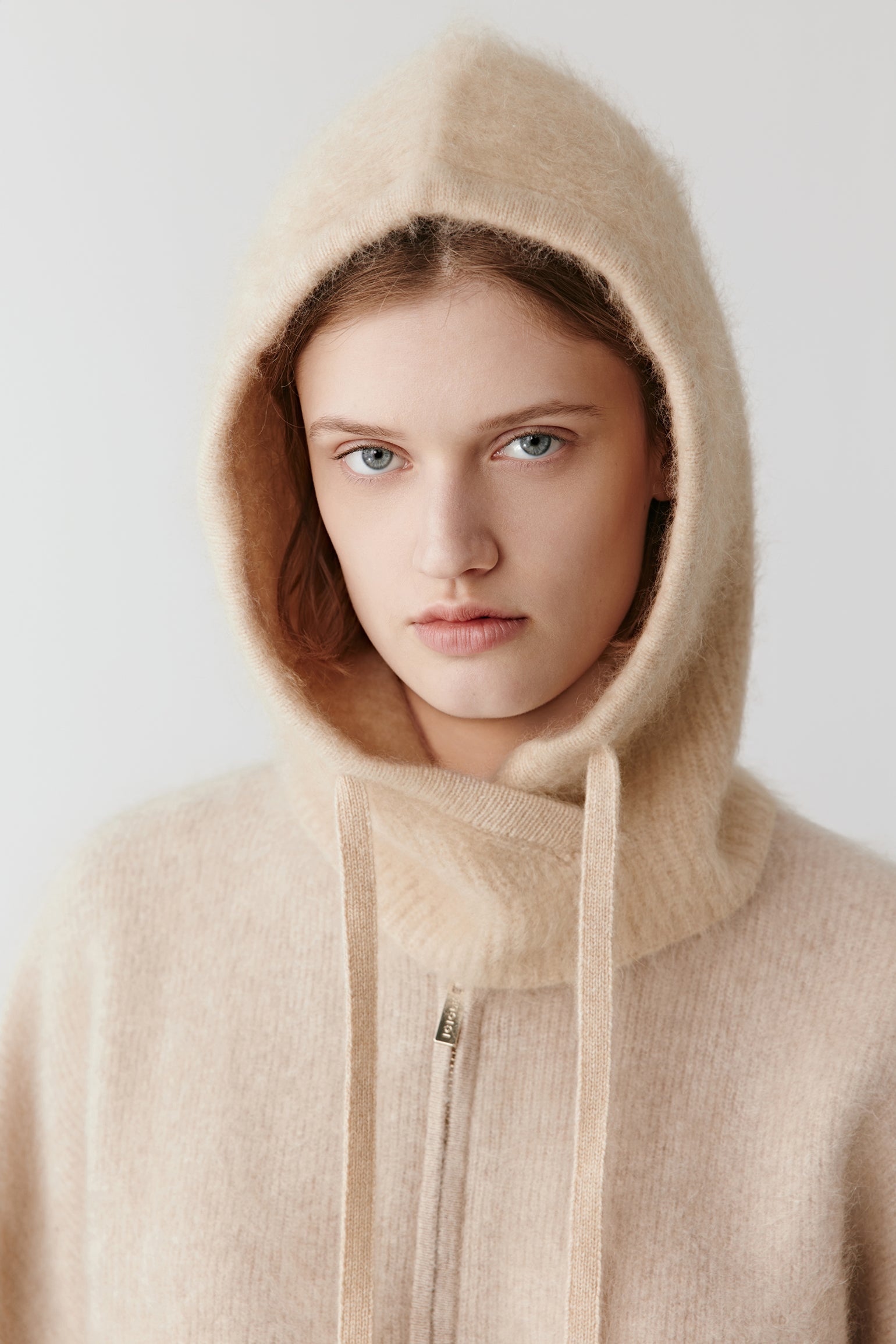 Woman wearing a beige knit hood with long drawstrings styled with a soft sweater on a light background