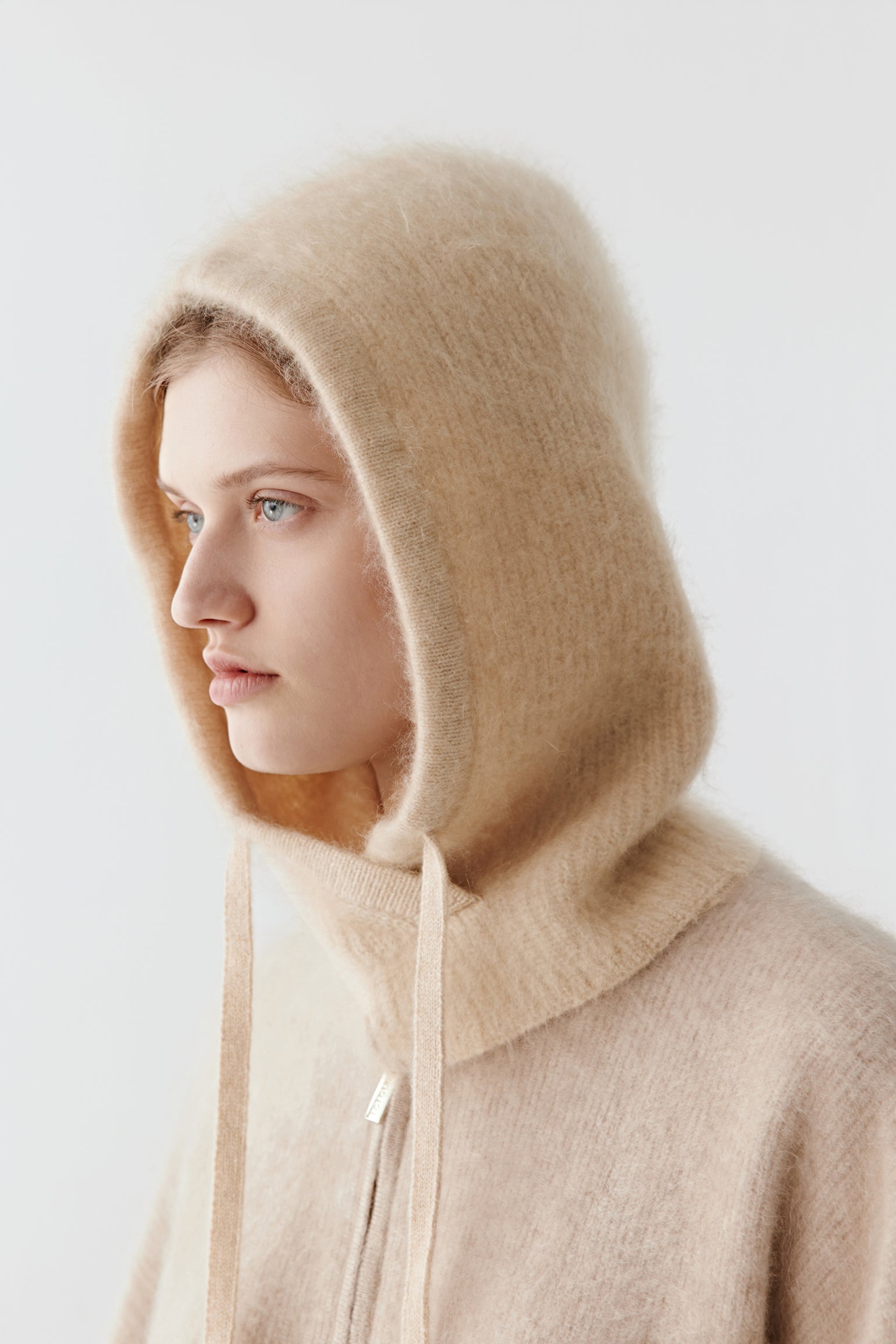Side view of a woman wearing a beige knit hood with long ties on a light background