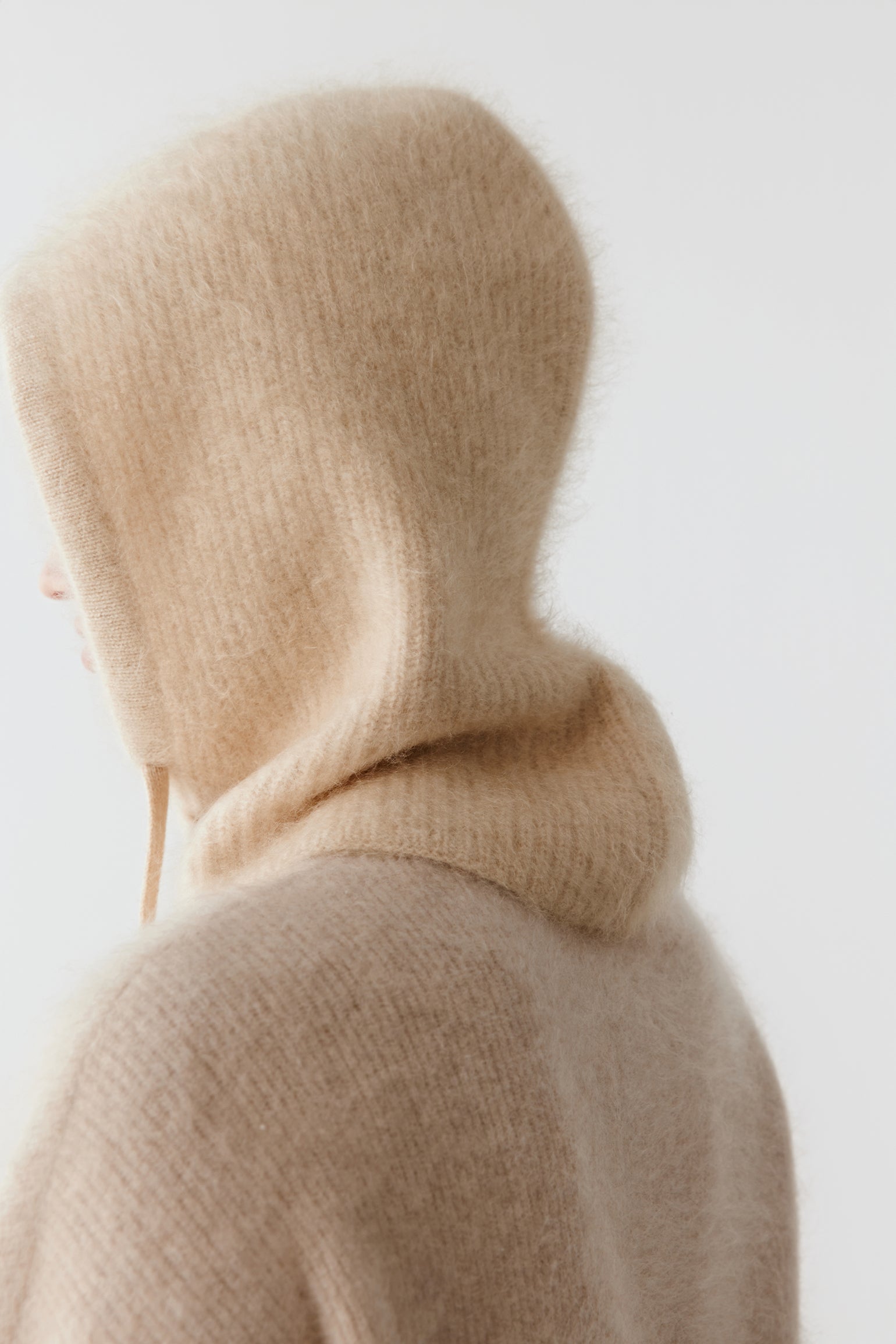Back view of a beige knit hood with long drawstrings on a light background