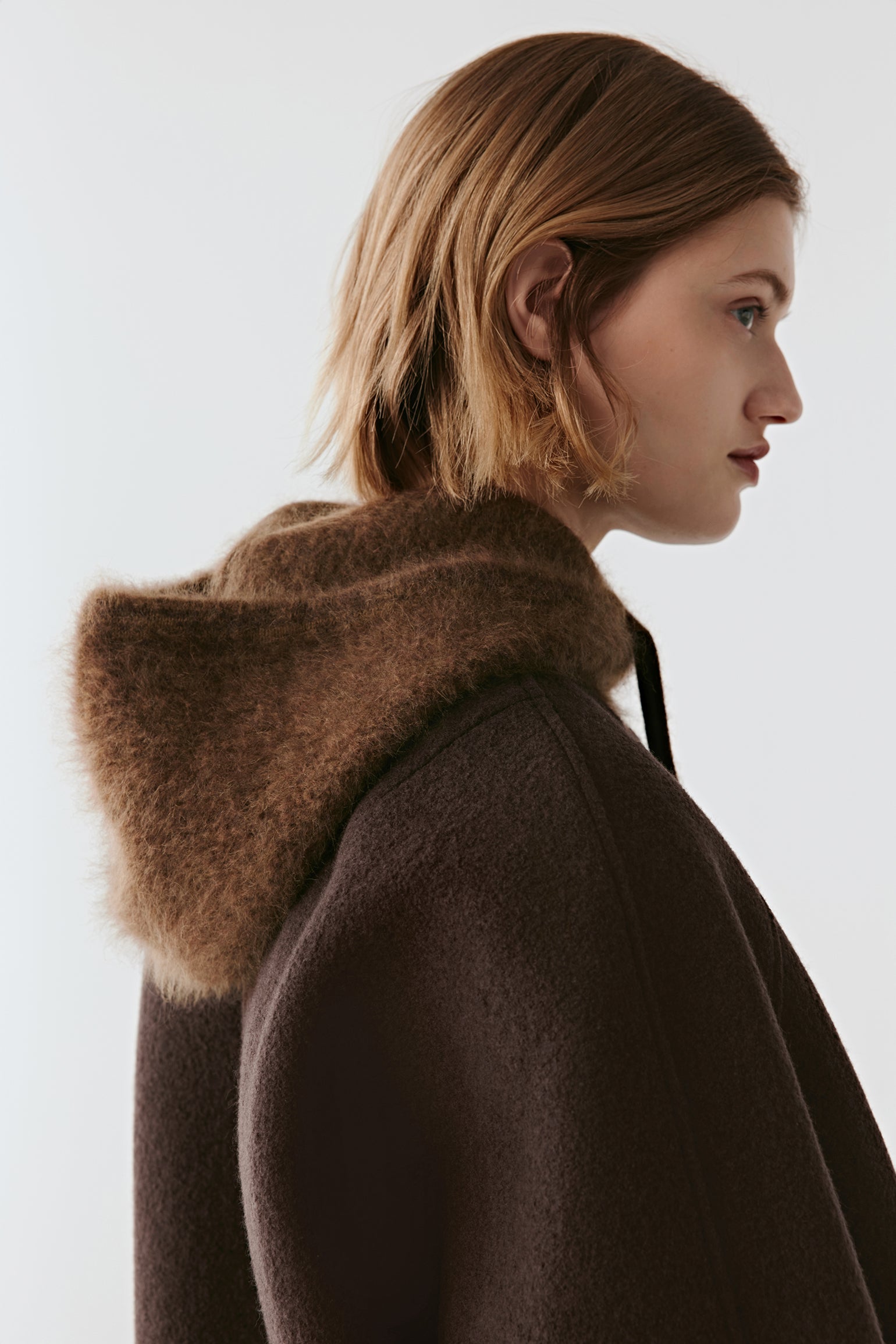 Back view of a brown knit hood with drawstrings over a dark coat on a light background