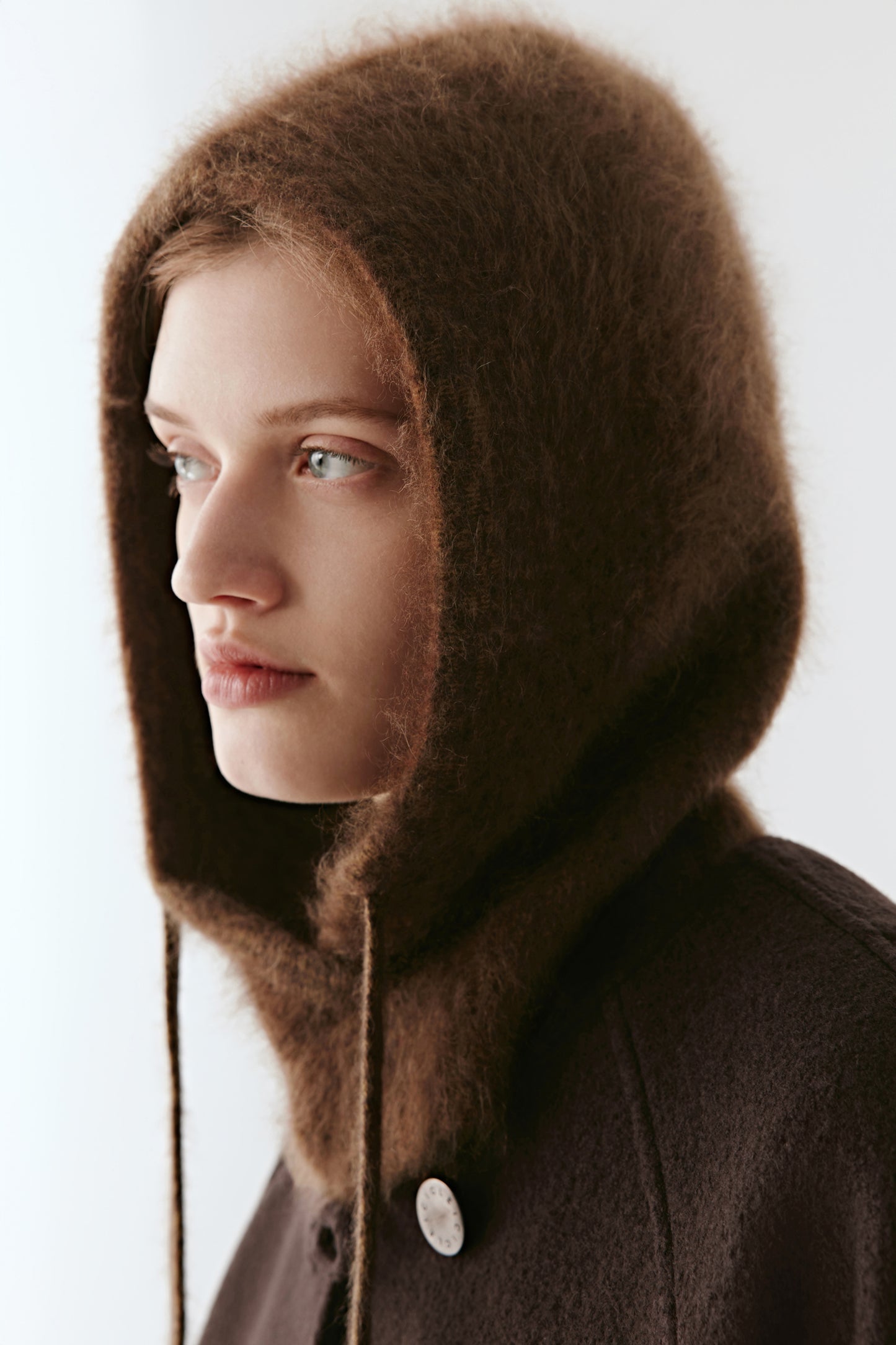 Side view of a woman wearing a brown knit hood with long ties on a light background