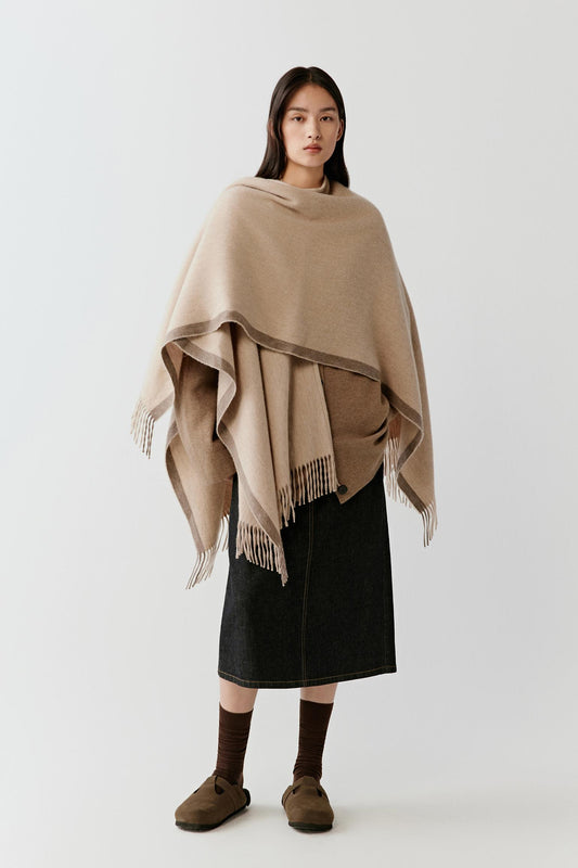 Model wearing the undyed beige cashmere shawl draped over the shoulders, styled over a midi skirt and knitwear.