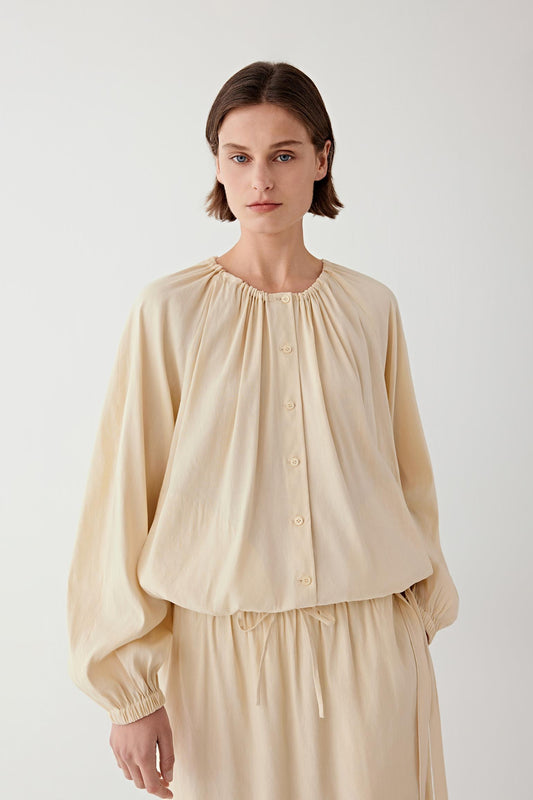 Front view showing the gathered neckline and the loose volume of the blouse through the body and sleeves.