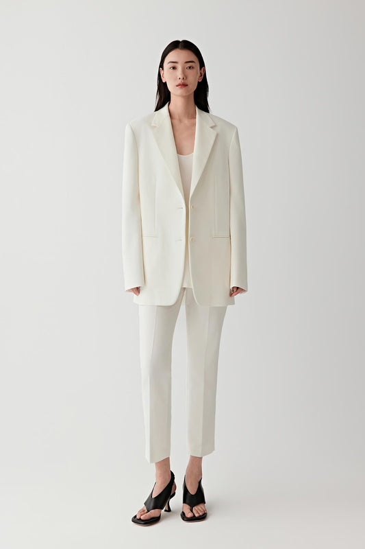 Full-length studio photograph showing the straight relaxed silhouette of the blazer worn over matching trousers.