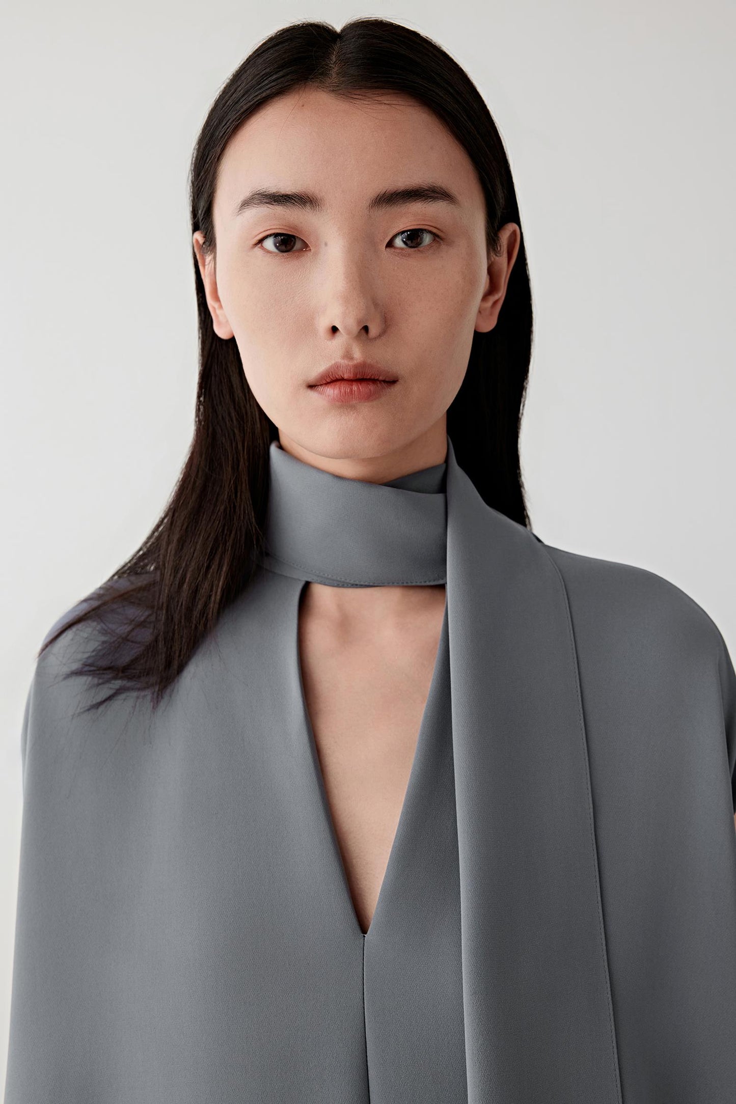 Close-up portrait focusing on the wrap neckline and upper construction, detailing the matte crepe surface, soft folds and subtle tonal variation of the grey shade.