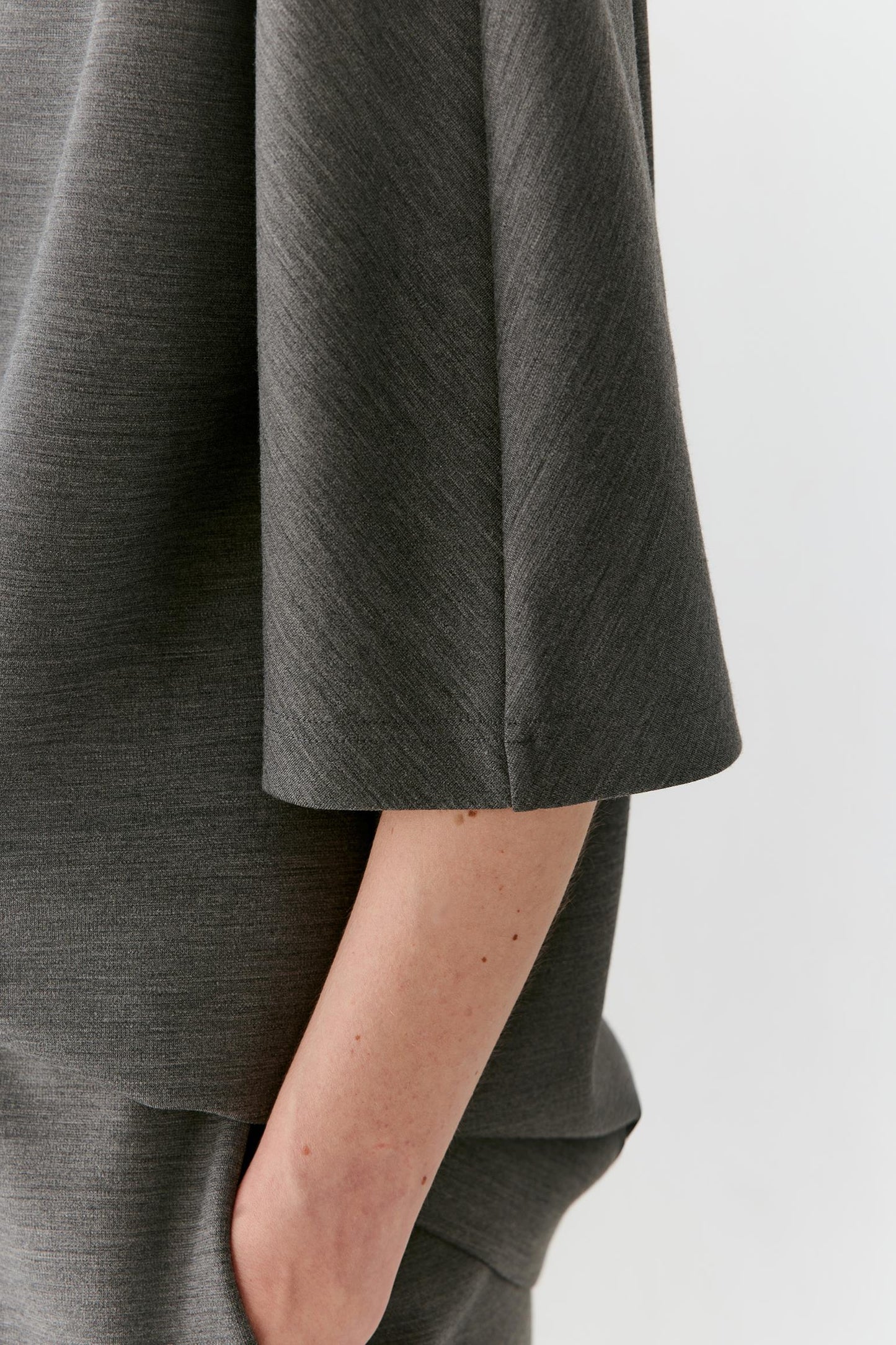 Close-up of a person wearing a dark gray textured top, showing the sleeve and side of the garment against a light gray background.