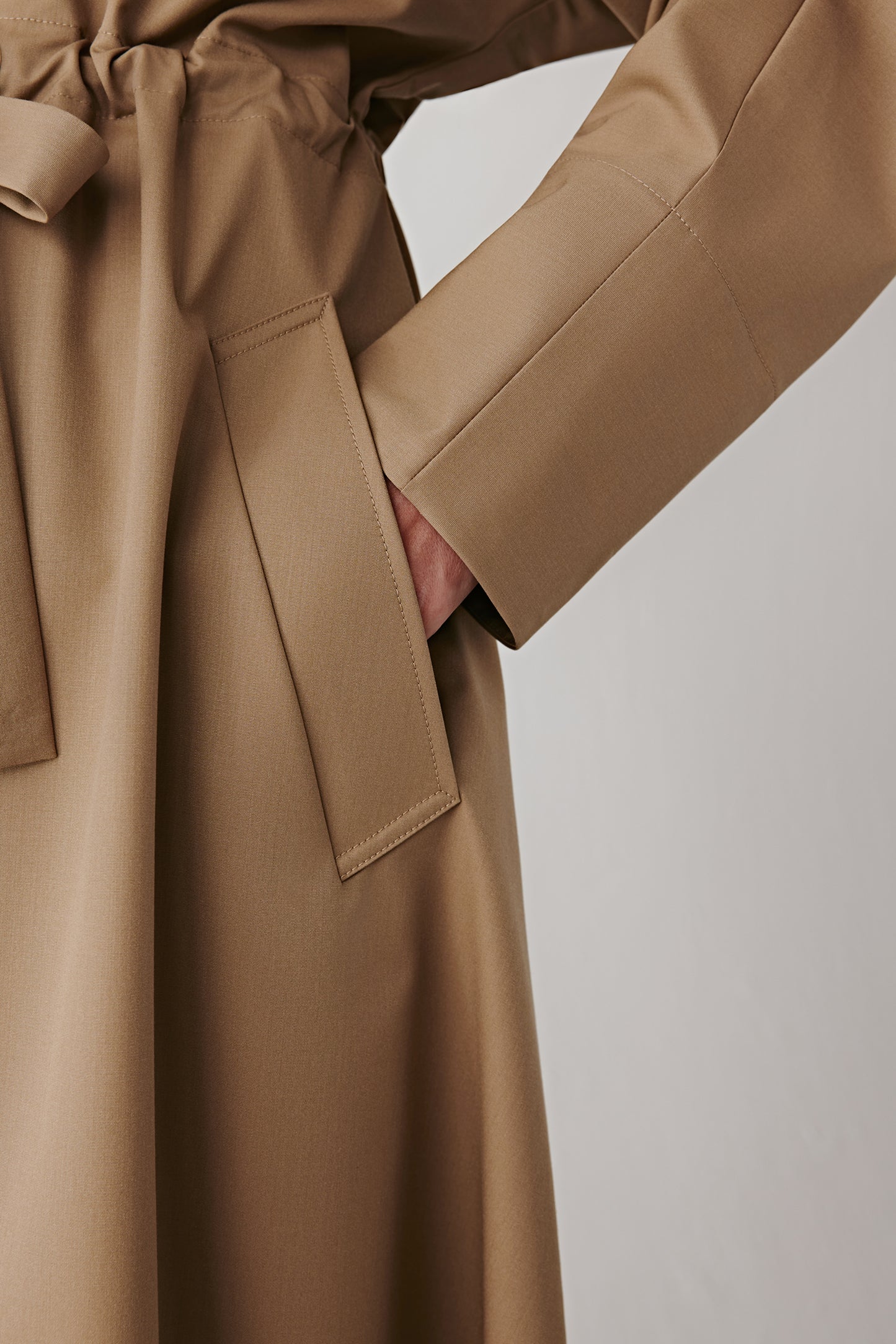 Detail shot of the tied belt and fabric texture of the beige coat, showing the refined finishing details.