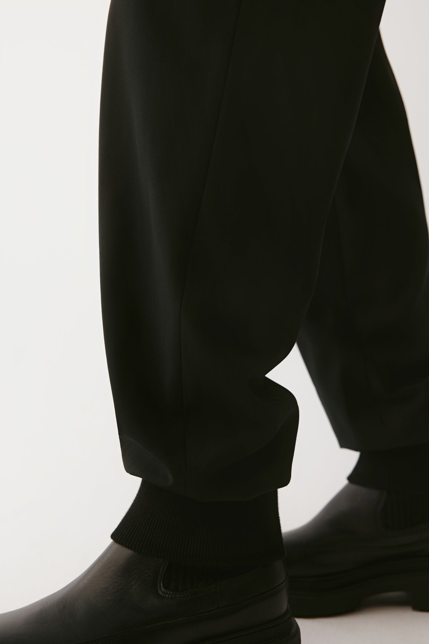 Detail of the lower leg and cuff highlighting the ribbed knit ankle finish that creates a clean taper. The smooth drape of the wool fabric contrasts subtly with the matte leather shoes.