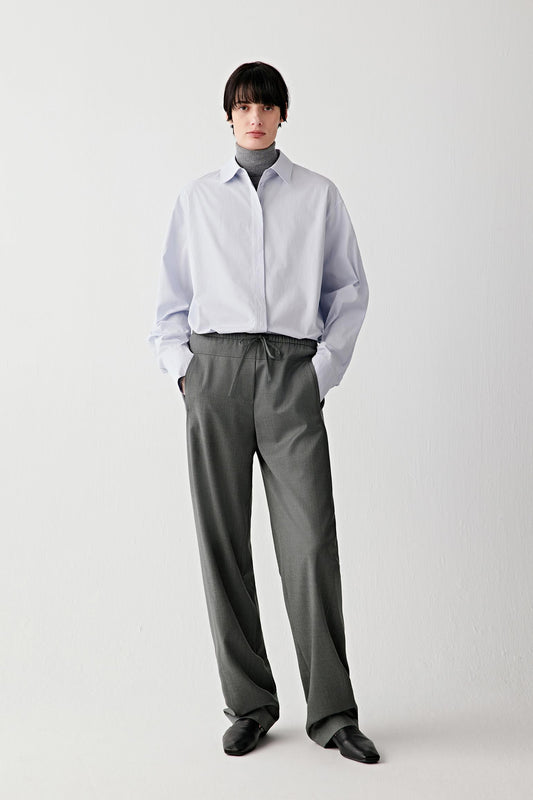 Full-length front view of a light blue cotton poplin shirt worn with grey trousers.