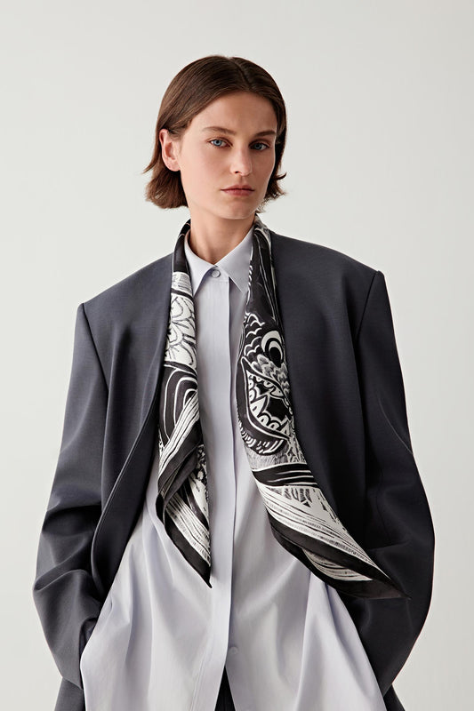 Three-quarter view showing the scarf styled over a grey suit, revealing the black and white illustration across the silk surface.