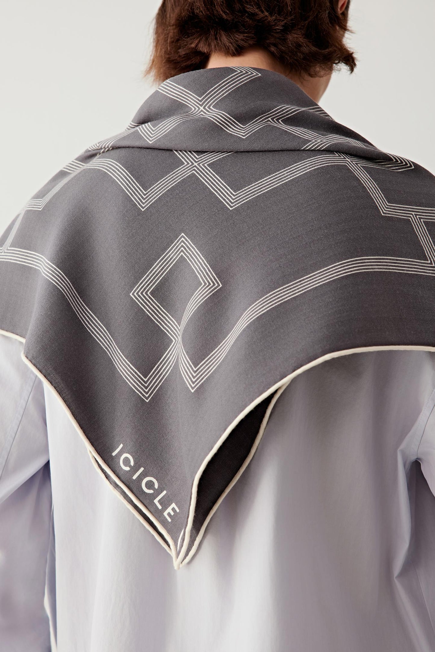 Close-up back view of the scarf worn around the shoulders, showing the fine cashmere and silk weave, precise edges, and the subtle contrast of the geometric pattern.