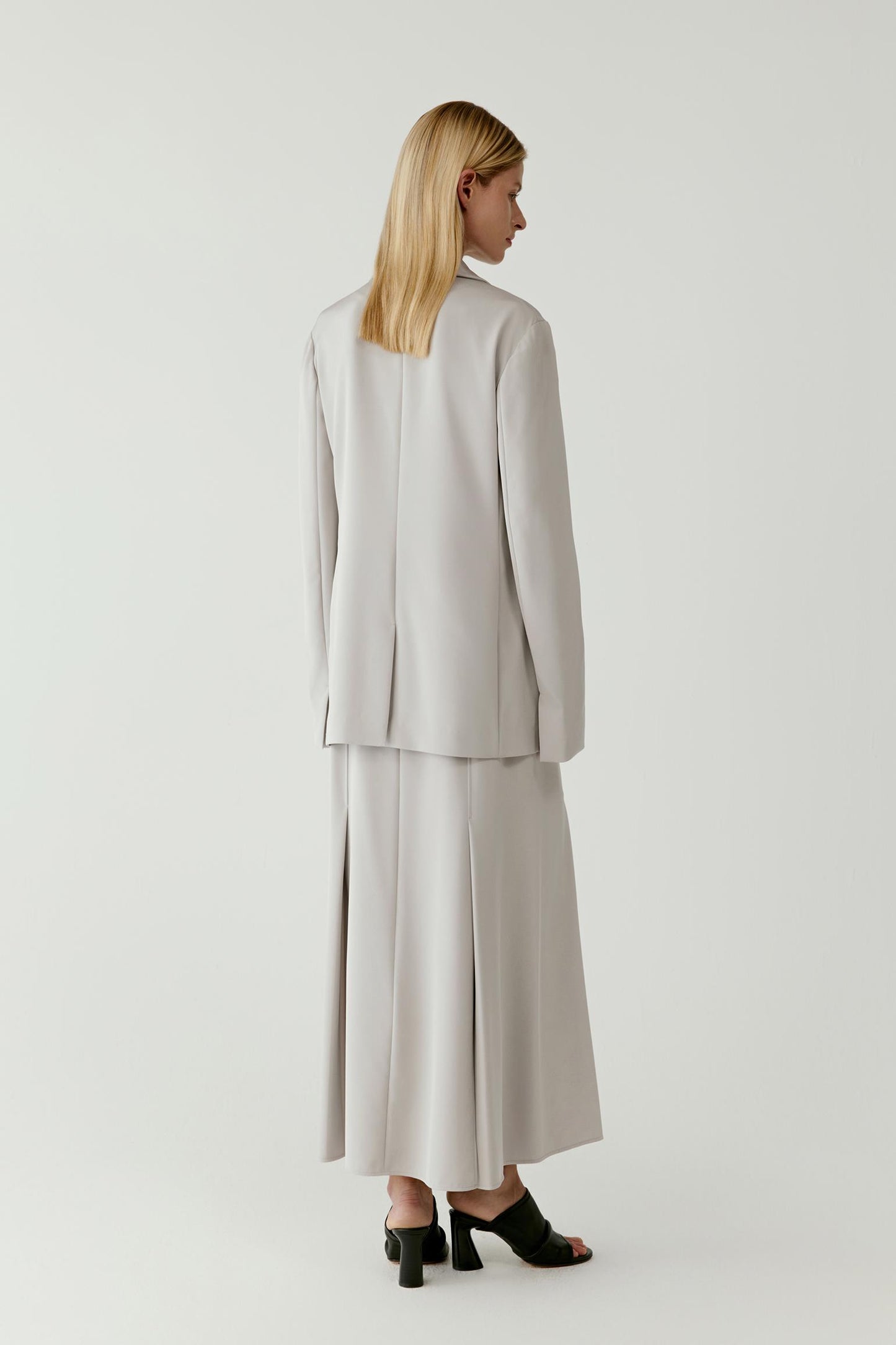 Full-length front view highlighting the inverted pleats, the gentle flare from the waist and the smooth, light-reflective surface of the silk fabric