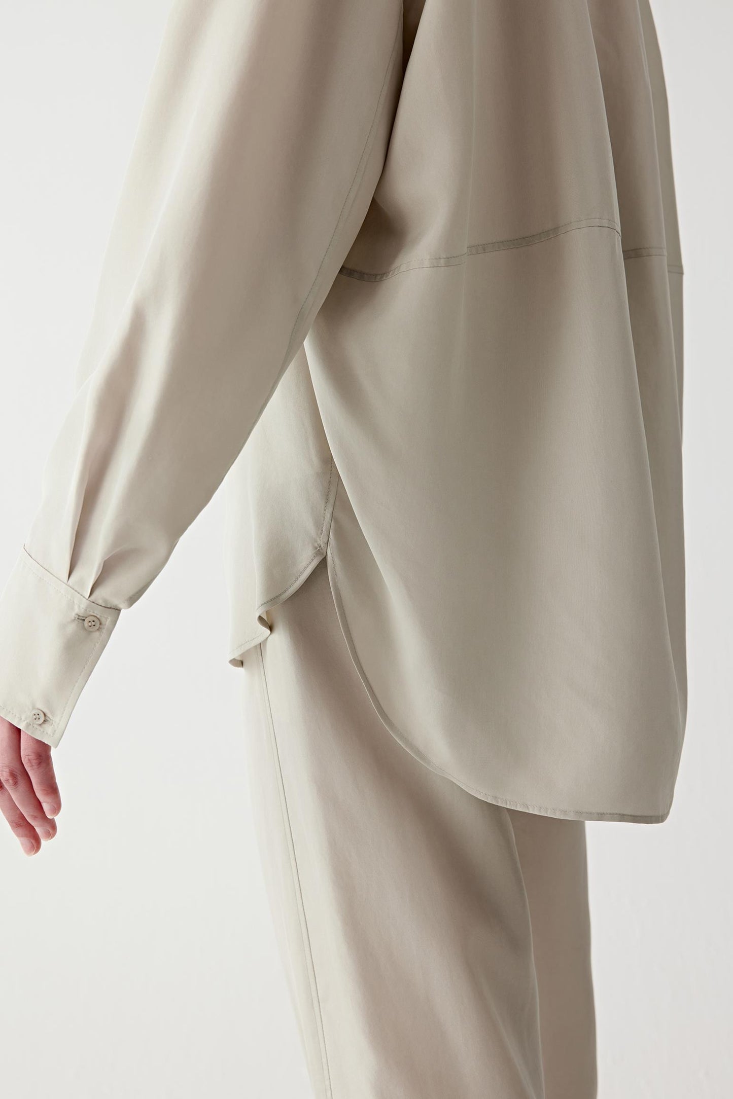 Close-up of the sleeve and cuff area, showing the clean finishing, seam lines and the lightweight structure of the fabric, with a soft, flowing drape