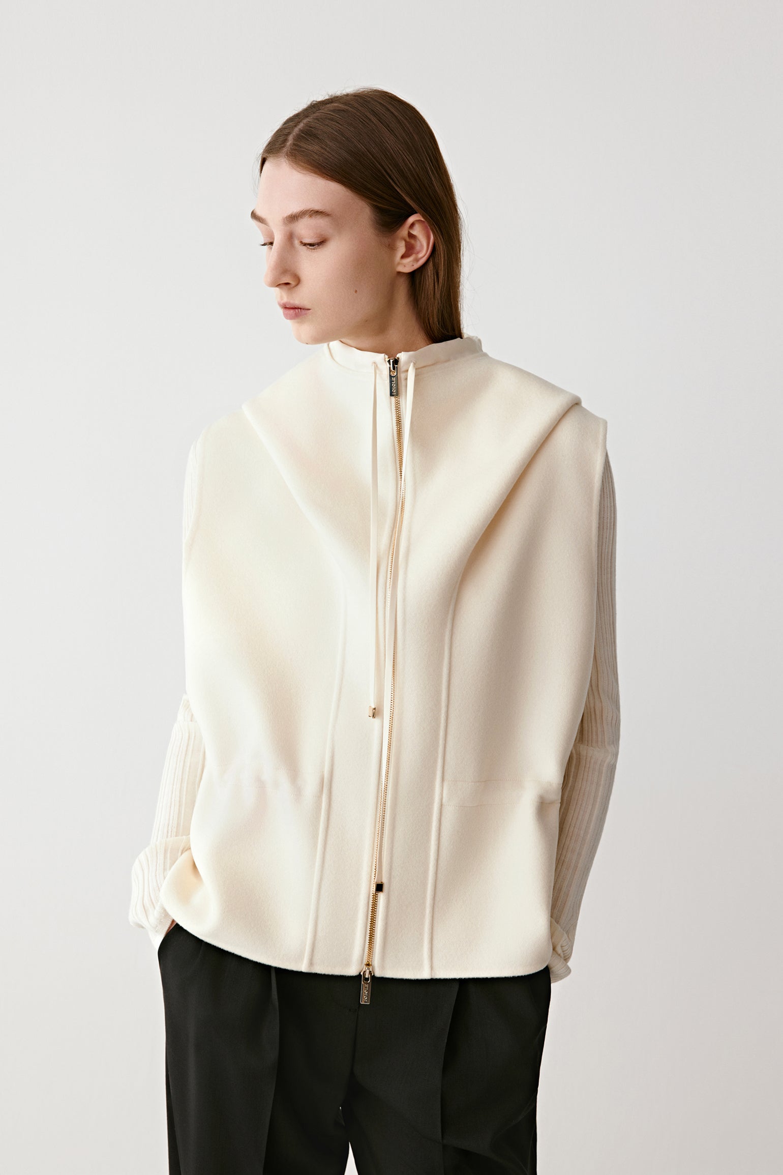 Front view of a woman wearing a cream sleeveless wool-cashmere coat over wide black trousers.