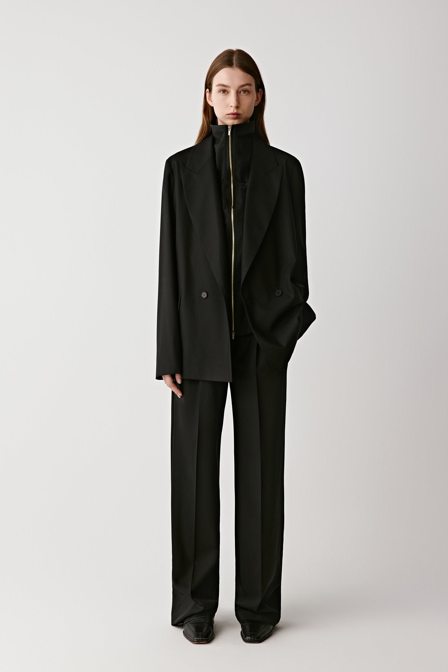 Front full-length view of a woman in a deep black twist wool blazer styled with matching trousers.
