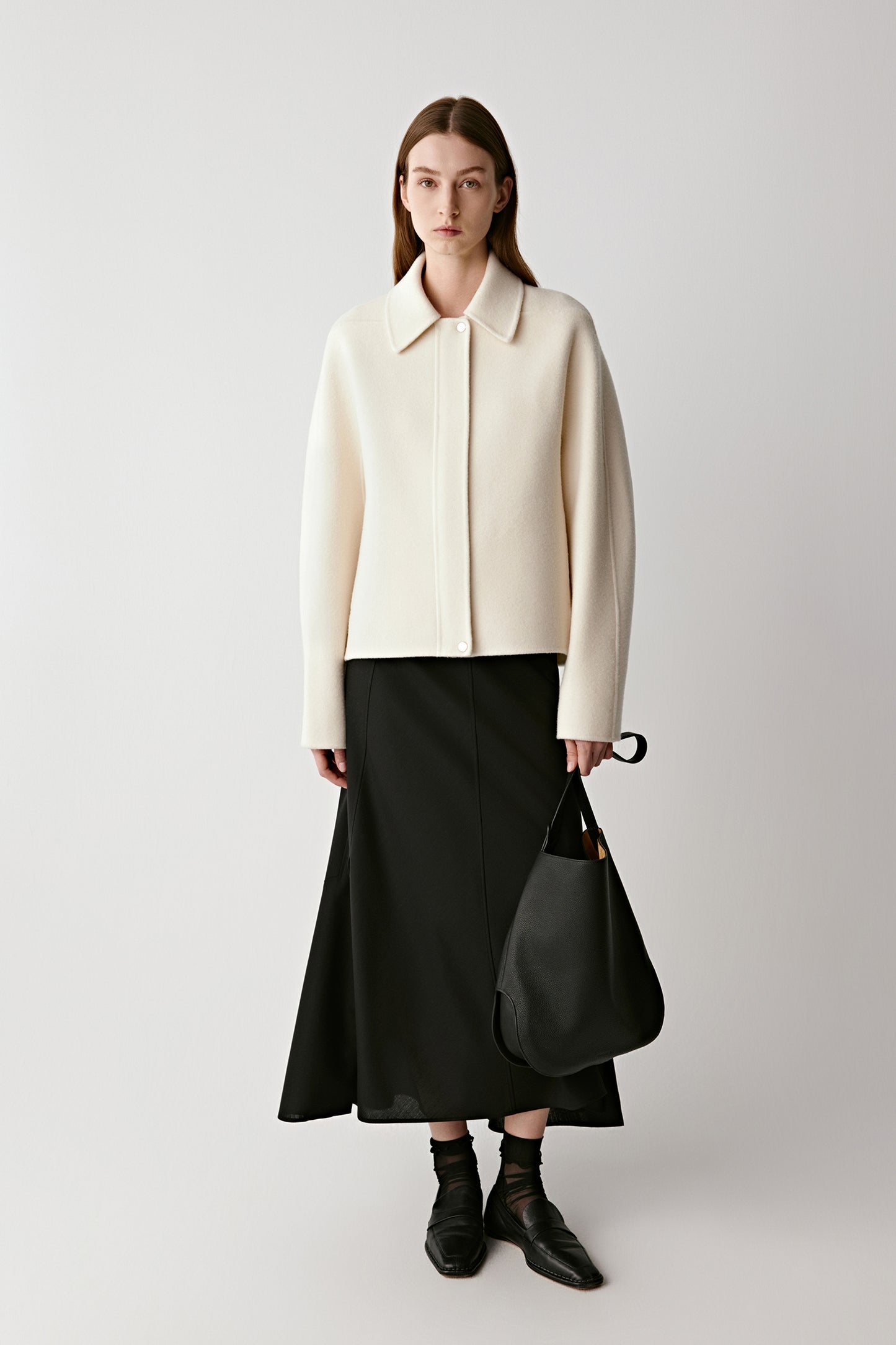 Front view of a woman wearing a cream wool-cashmere coat paired with a black skirt and boots.
