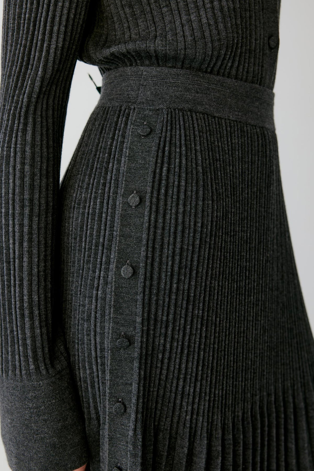 Close-up of the grey melange pleated wool skirt, highlighting the elasticated waistband and side button detailing.