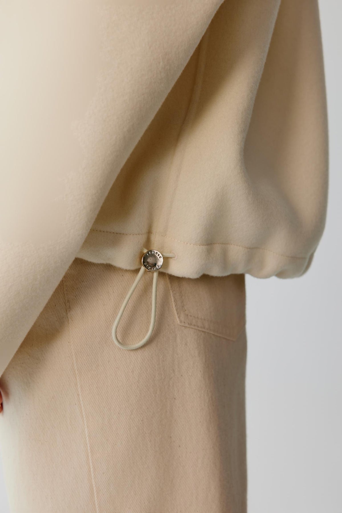 Close-up highlighting the adjustable drawstring at the hem and relaxed construction of the cream wool cashmere jacket.