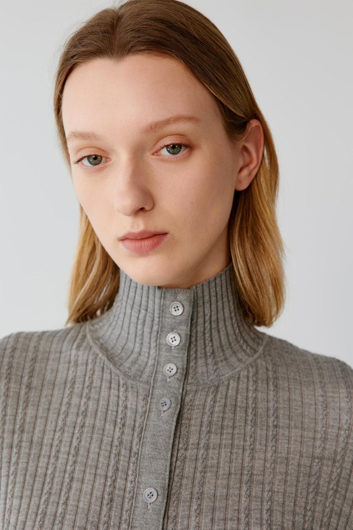Close-up highlighting the stand collar, button-front fastening and ribbed texture of the grey melange worsted wool cardigan.